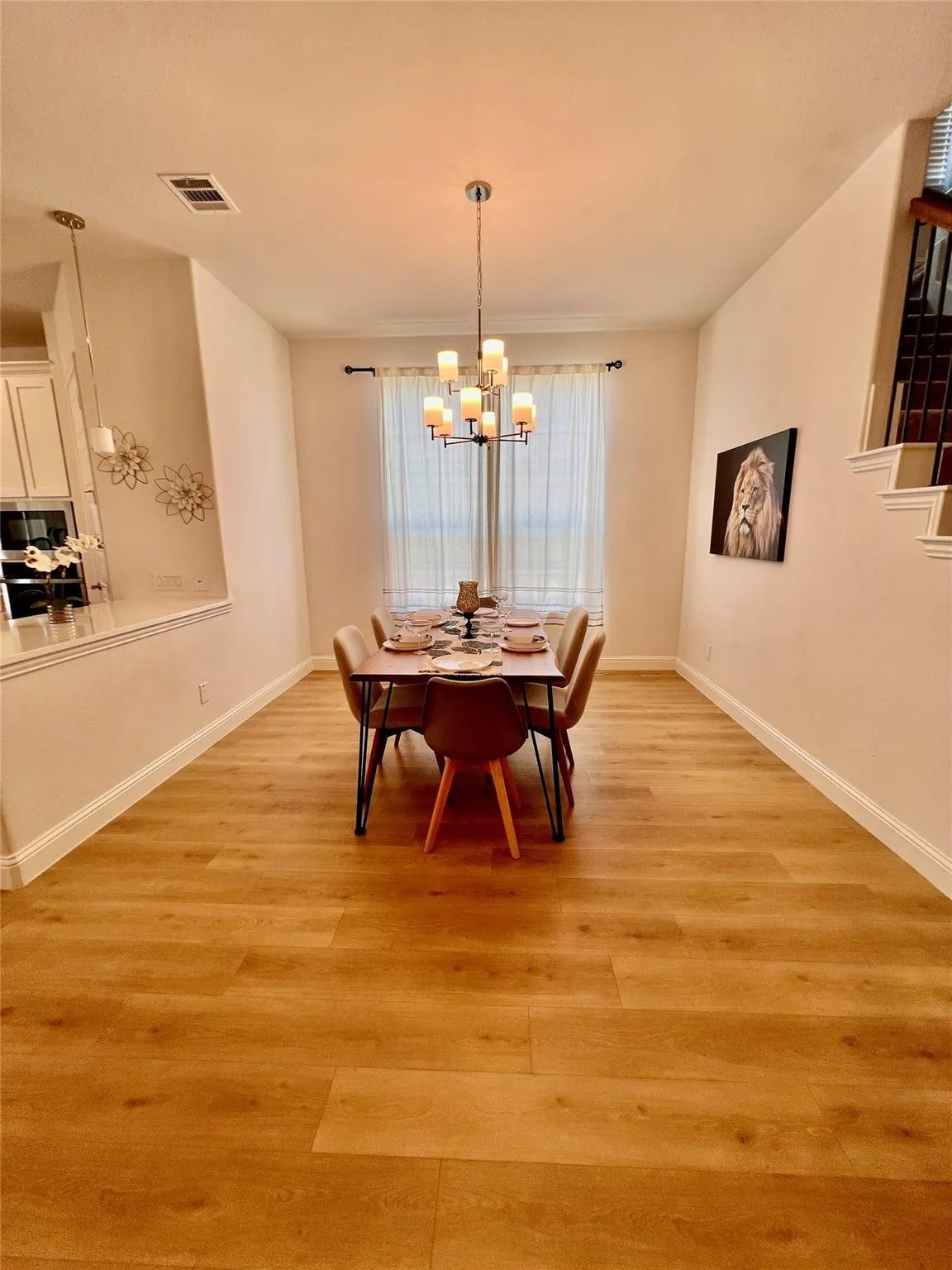 Dining area featuring wood-finish flooring, a contemporary chandelier, and a window with sheer curtains