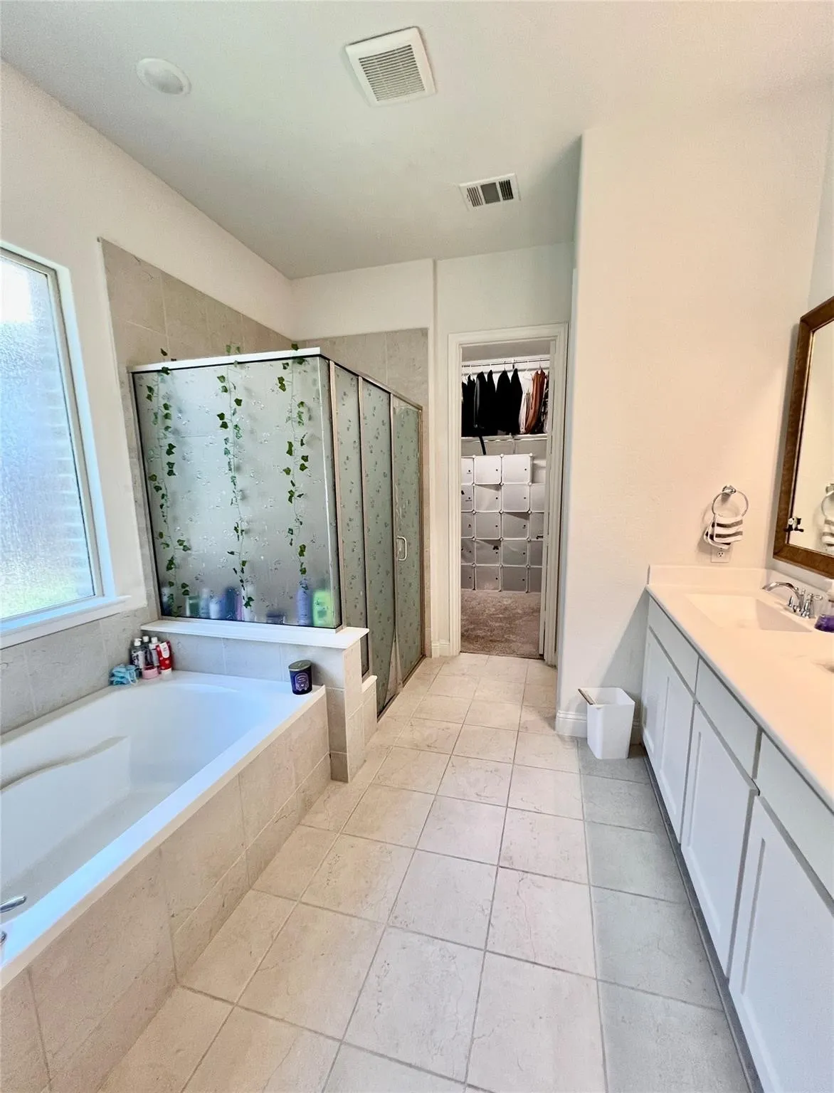 Spacious bathroom featuring a built-in soaking tub, a separate shower enclosure, a dual-sink vanity with white cabinetry, and light-toned tile flooring
