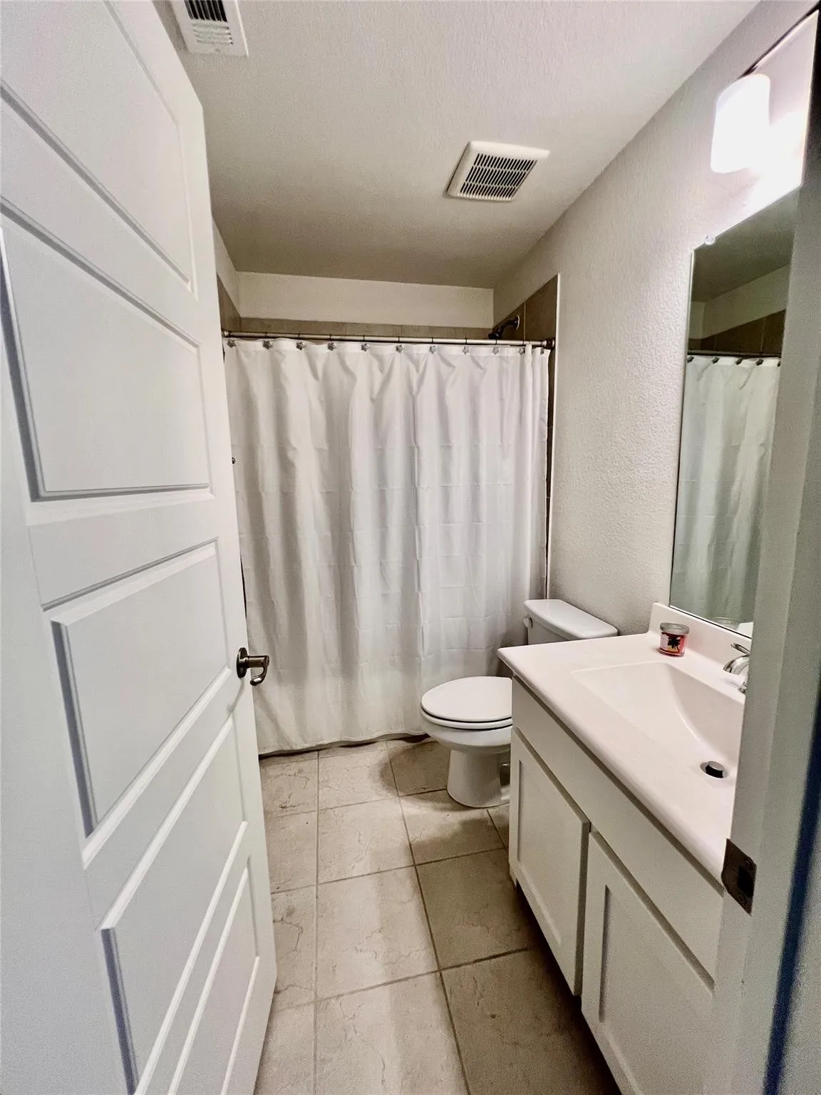 Bathroom featuring tile flooring, a shower-tub combination with tiled surround, a white vanity with integrated sink, and white cabinetry