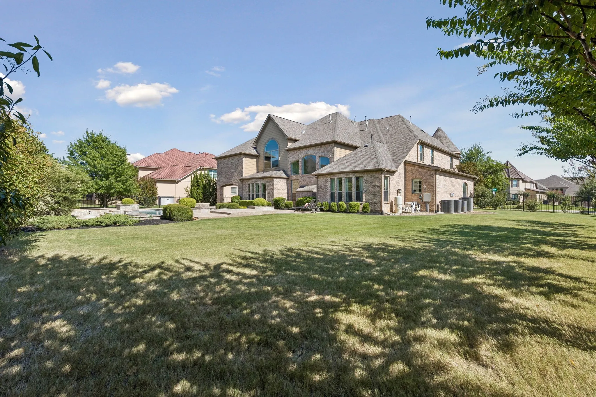 Expansive rear grounds featuring a brick exterior with multiple gables, extensive lawn, and a hardscaped patio area
