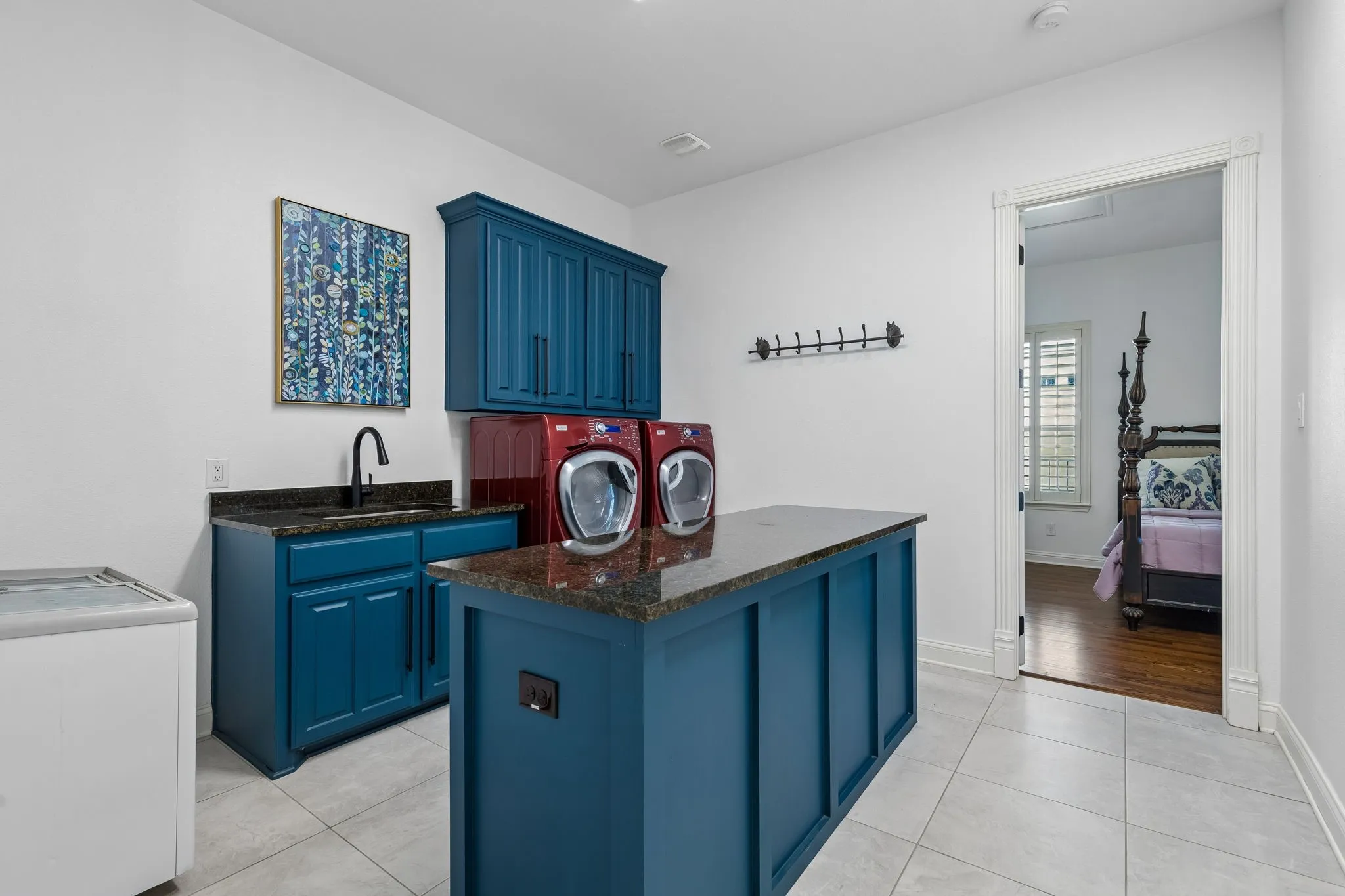 Massive laundry room featuring navy blue cabinetry, island with storage and plenty of space for folding, a sink and room for a freezer make this the ideal utility room.