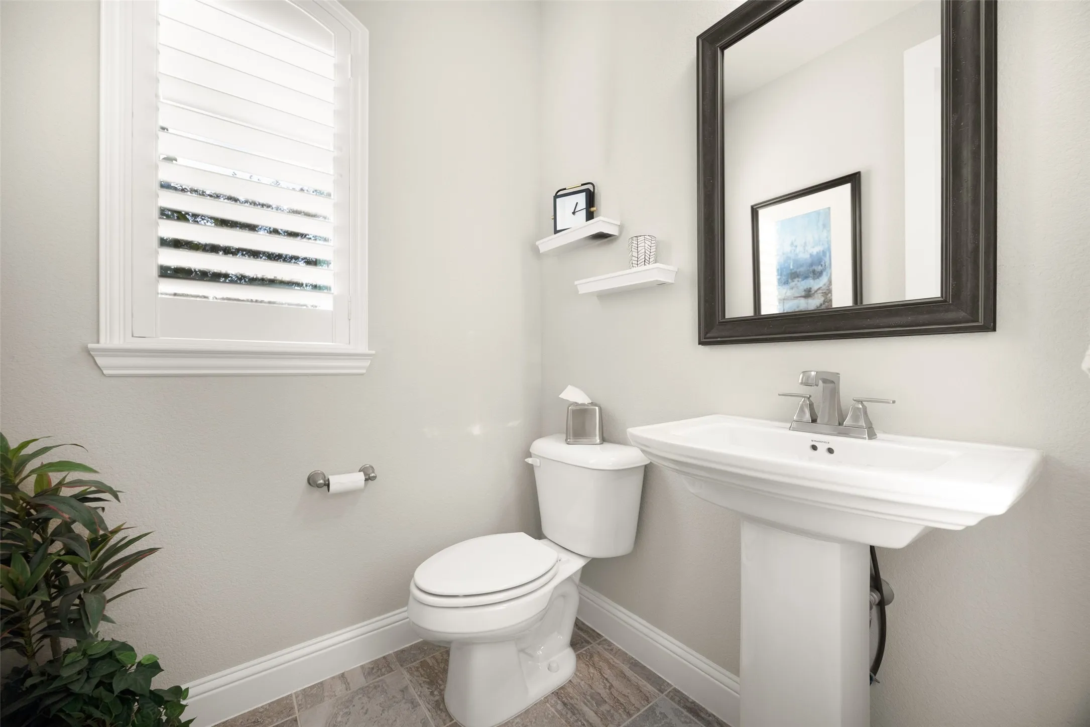 Pedestal sink with chrome faucet, complemented by a framed mirror