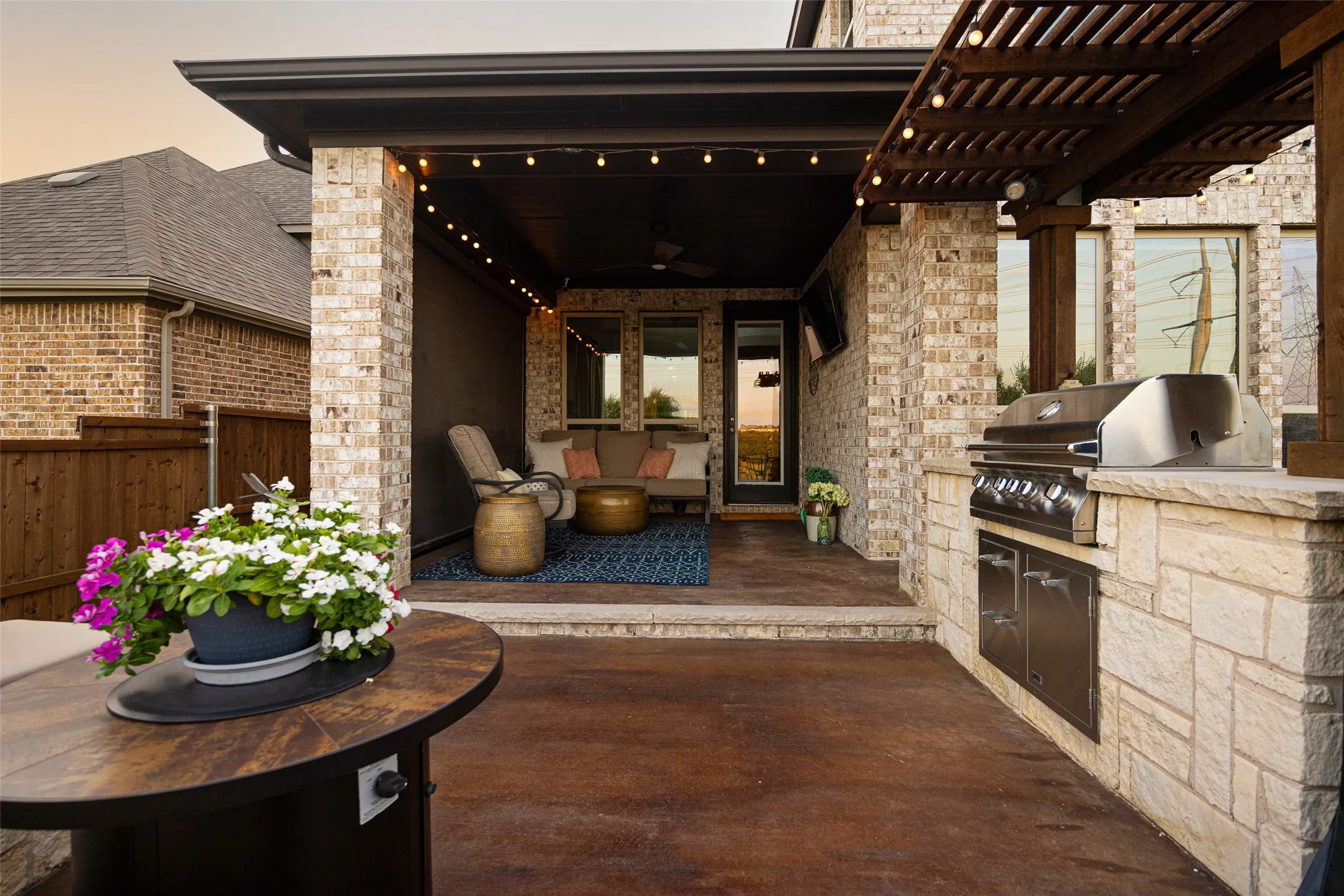 Custom electronic phantom shades. Covered patio with a built-in outdoor kitchen, pergola accent, stained concrete flooring, and string lighting