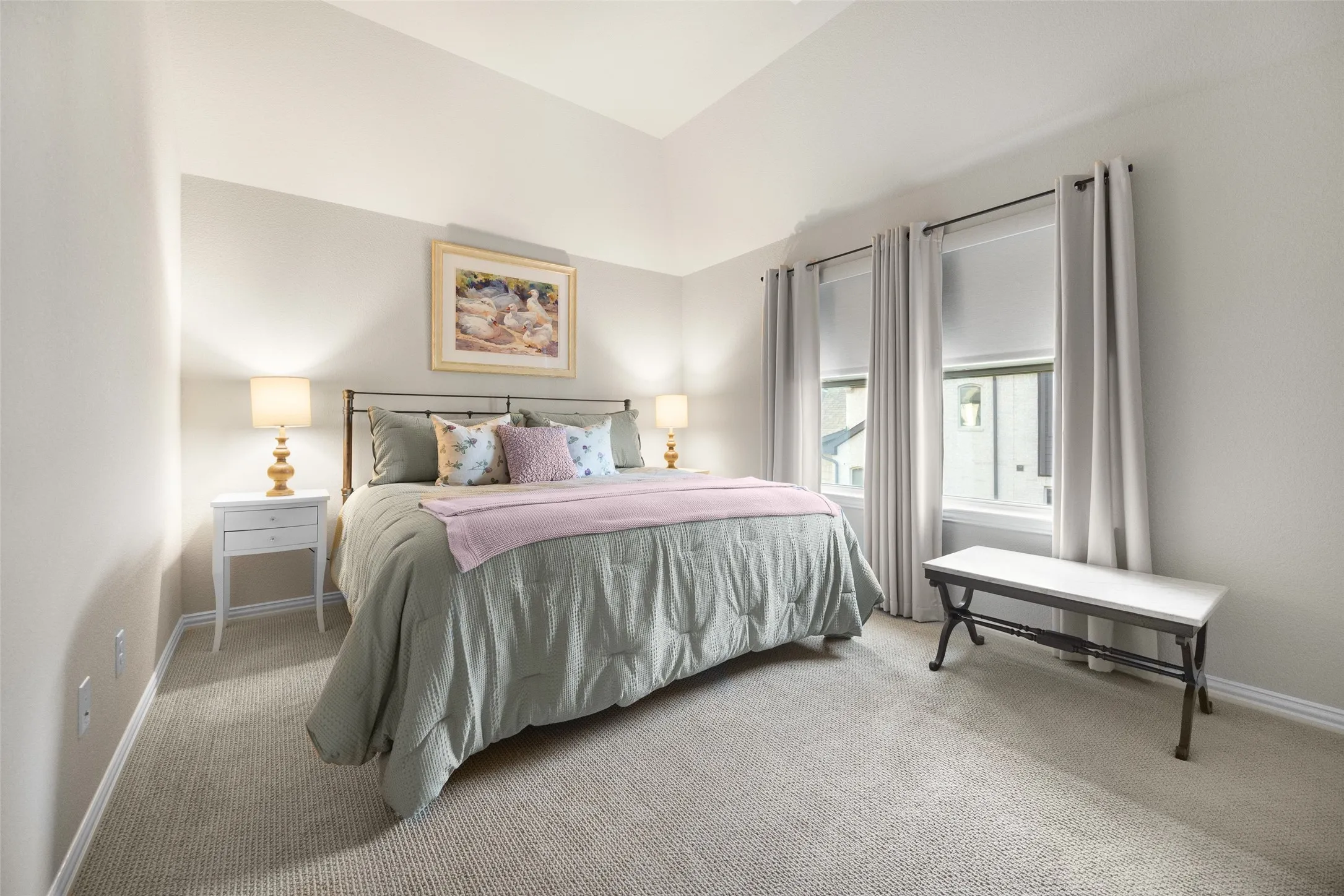 Carpeted room featuring a vaulted ceiling and two large windows with roller shades and drapery