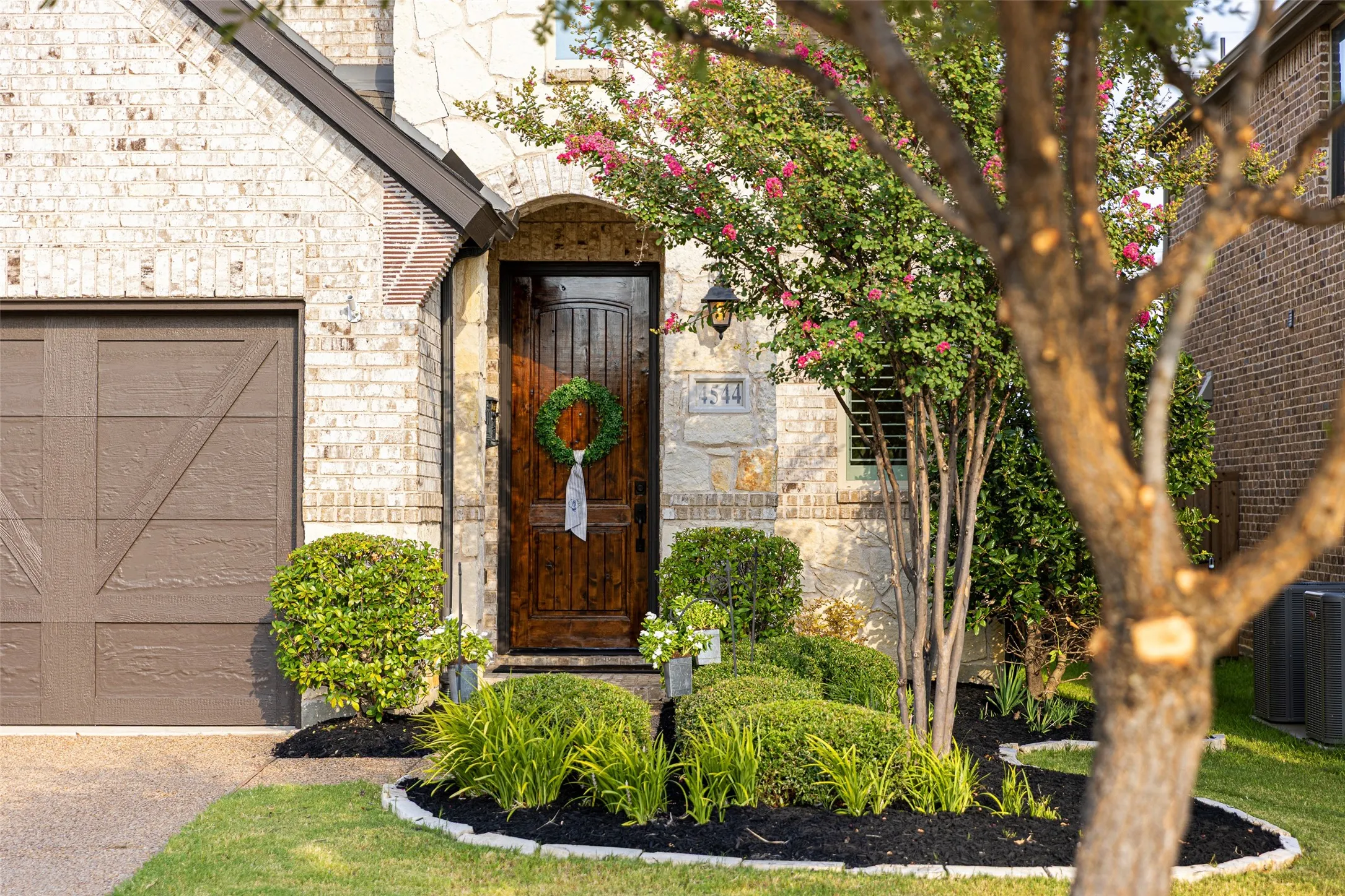Arched entryway with a dark wood door, stone and brick exterior, and a brown garage​​‌​​​​‌​​‌‌​‌‌​​​‌‌​‌​‌​‌​​​‌​​ door