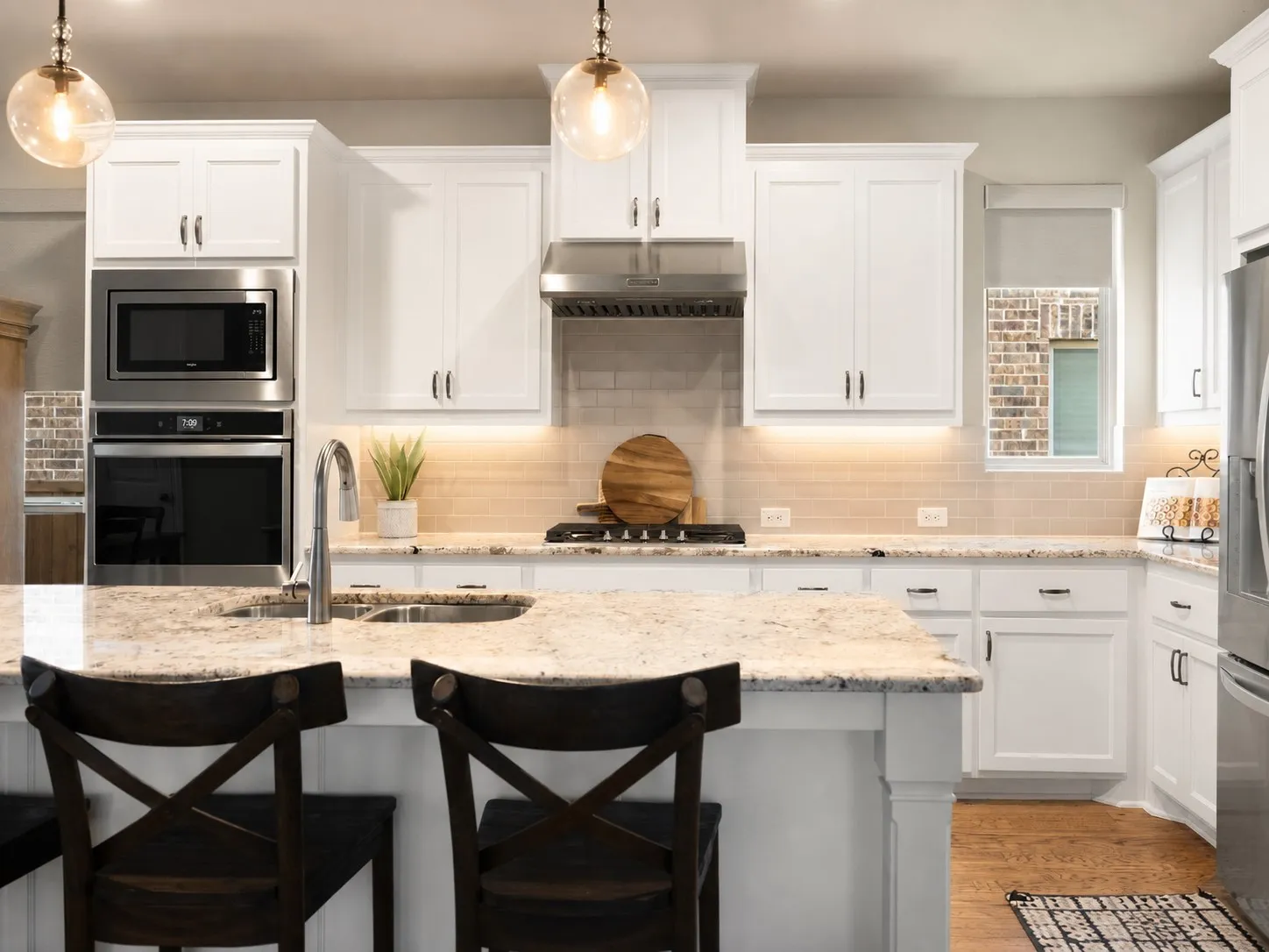 Modern kitchen featuring white cabinetry, light granite countertops, stainless steel appliances, a tile backsplash, and wood-finish flooring