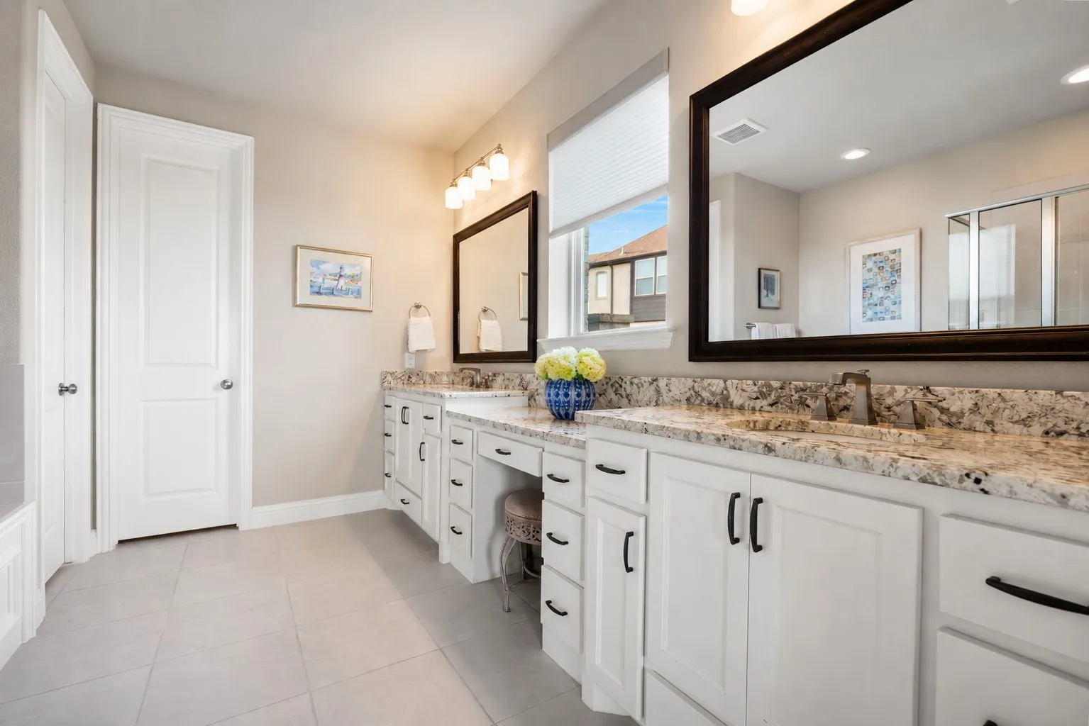 Double vanity featuring white shaker-style cabinetry, dark hardware, and stone countertops with integrated sinks