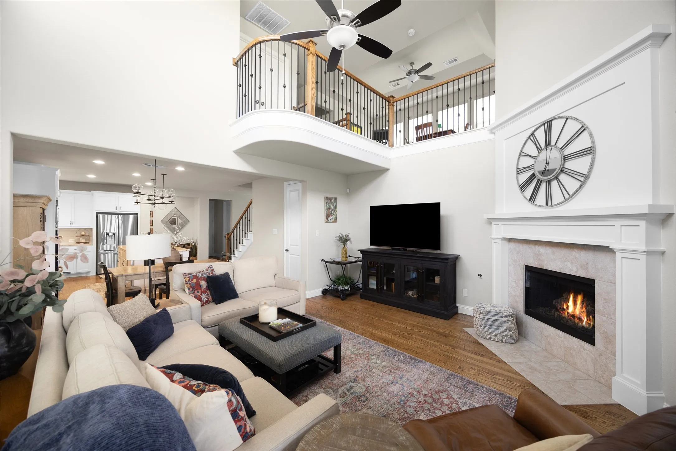 Vaulted living room featuring a gas fireplace with a stone surround, a wrought iron balcony overlooking the space, wood-finish flooring, and recessed lighting