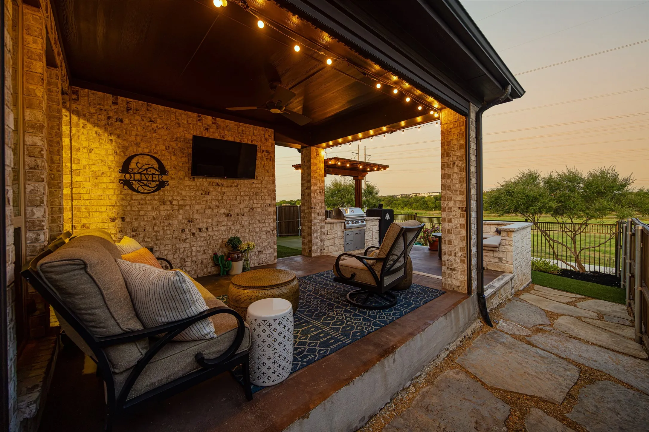 Covered outdoor patio featuring a brick accent wall, built-in outdoor kitchen with grill, wood-finish ceiling with string lights, and flagstone patio