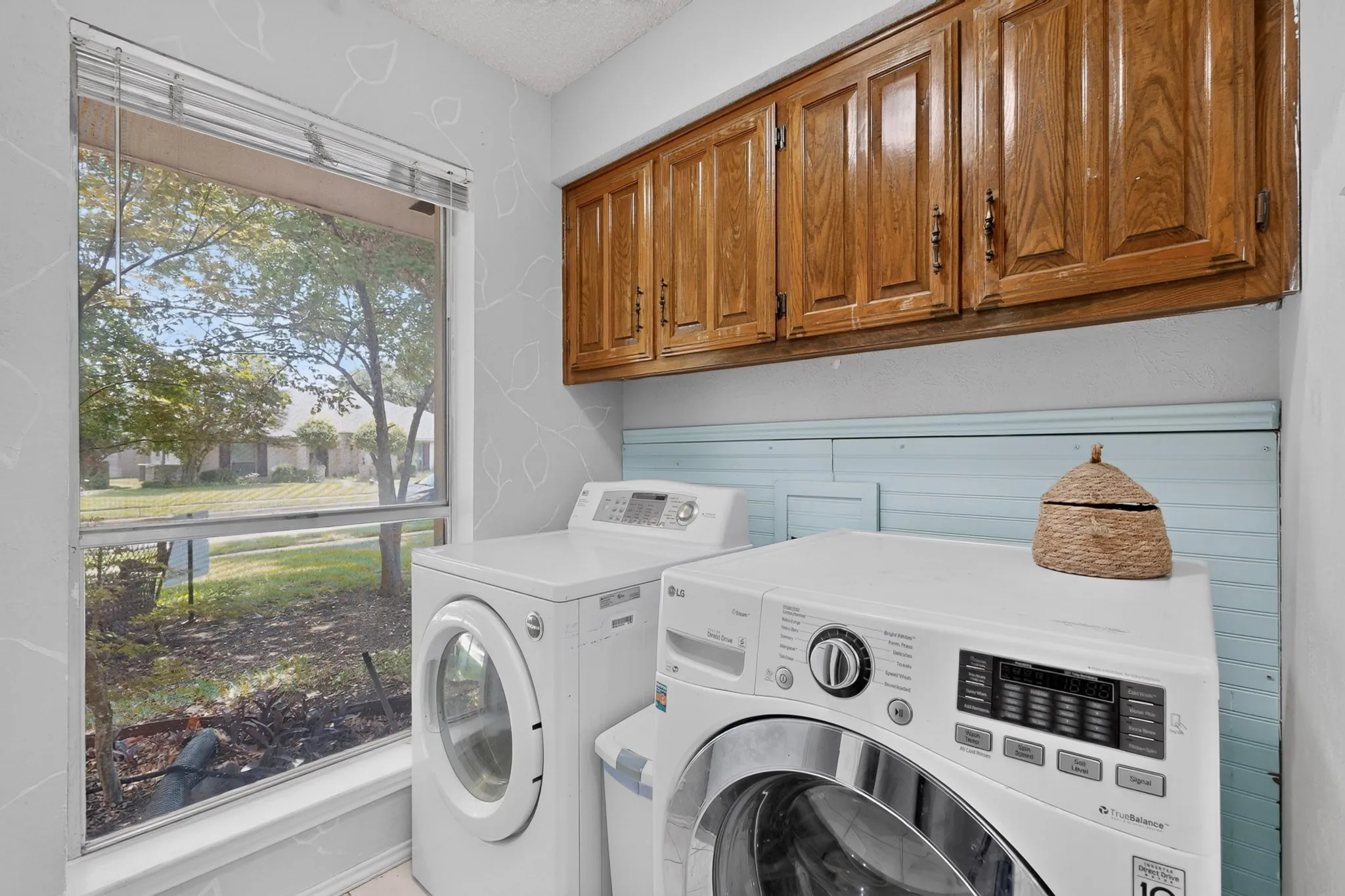 Laundry area featuring wood cabinetry, light blue wainscoting, and a large window overlooking green space