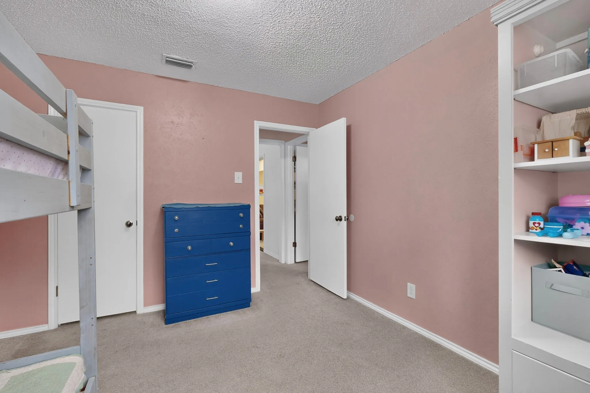 Interior room with textured ceiling, light pink walls, light gray carpeting, white trim, and a built-in white shelving unit