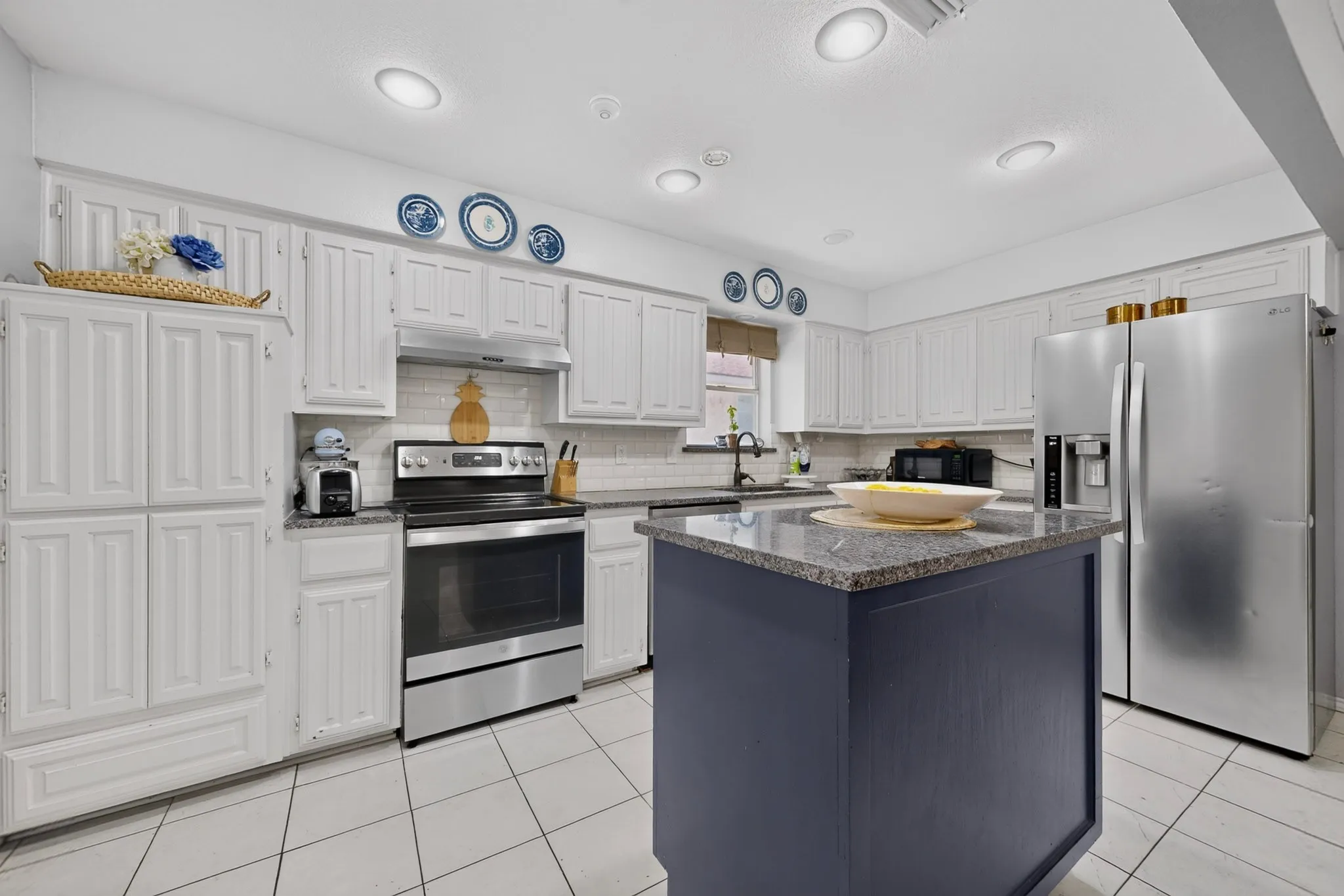 Kitchen featuring a movable central island with a stone countertop, white cabinetry, subway tile backsplash, stainless steel appliances, and recessed lighting
