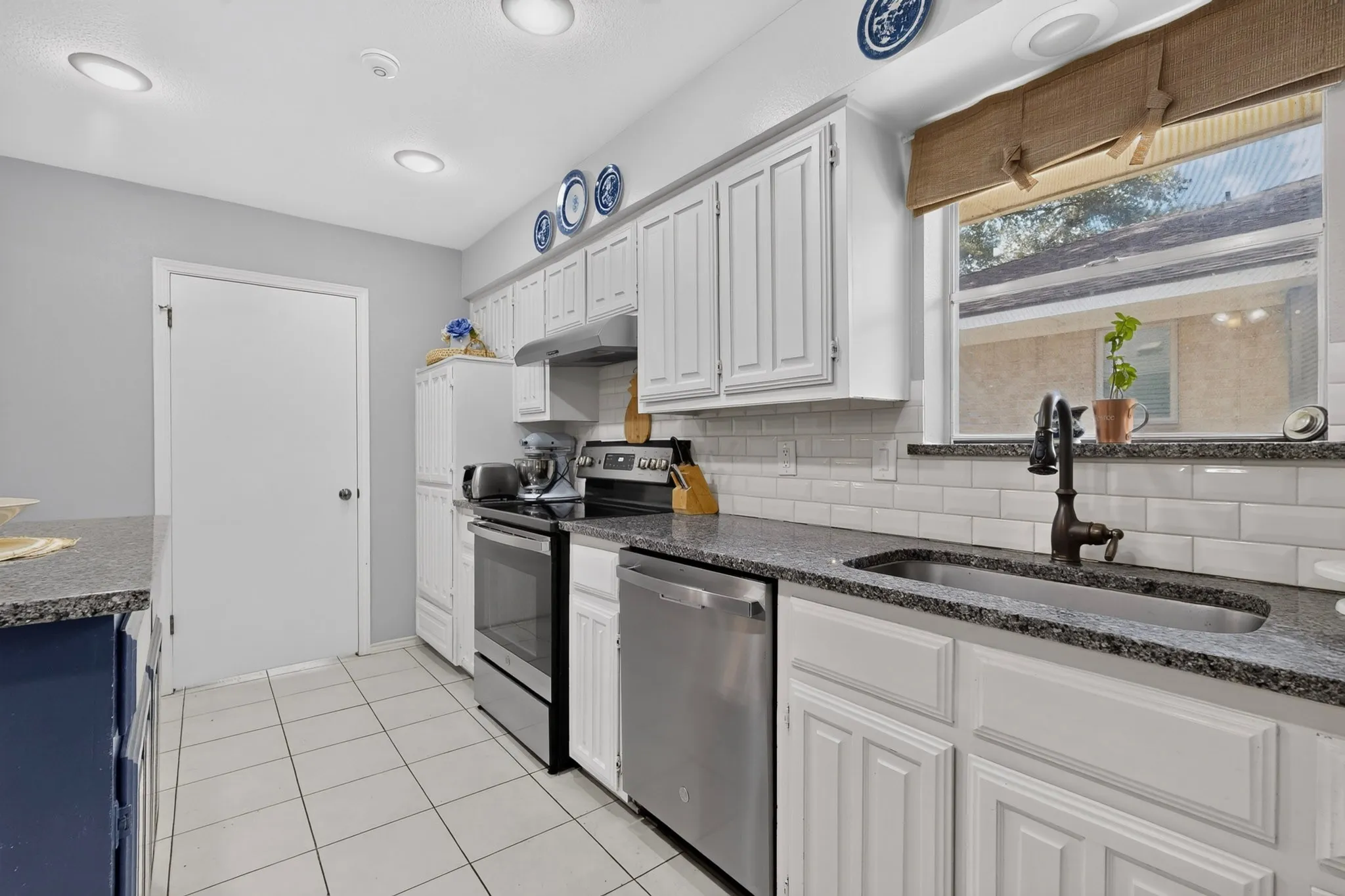 Contemporary kitchen featuring white cabinetry, subway tile backsplash, dark speckled countertops, stainless steel appliances, and tile flooring