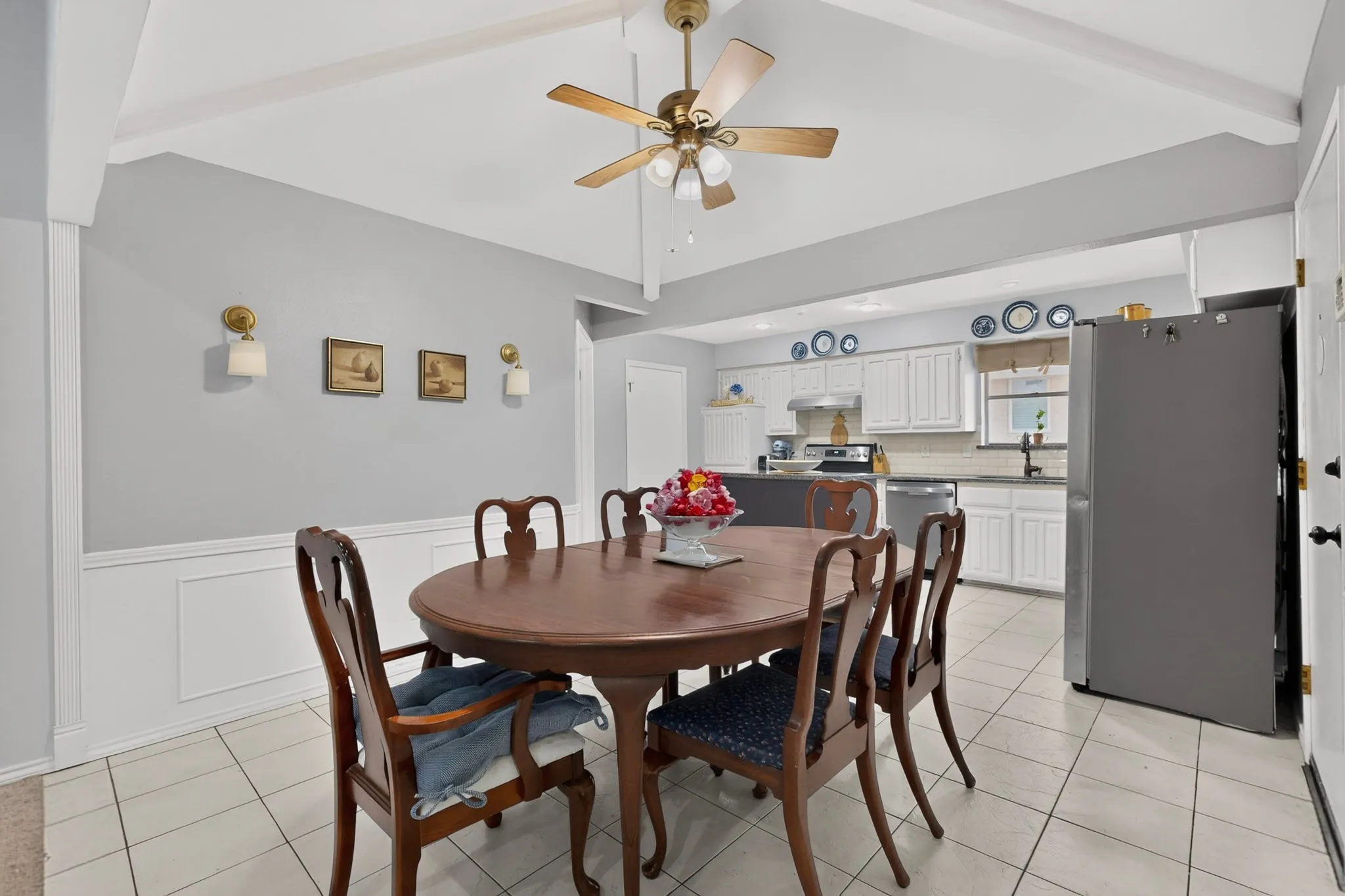 Dining area featuring light gray walls with white wainscoting, white tile flooring, and a ceiling fan with light fixture