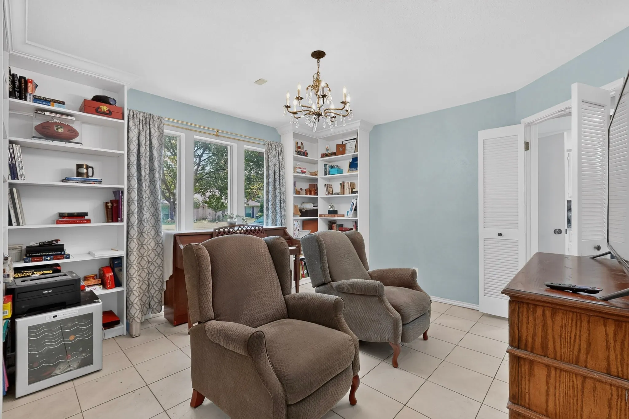 Room featuring white built-in shelving, tile flooring, and a chandelier light fixture