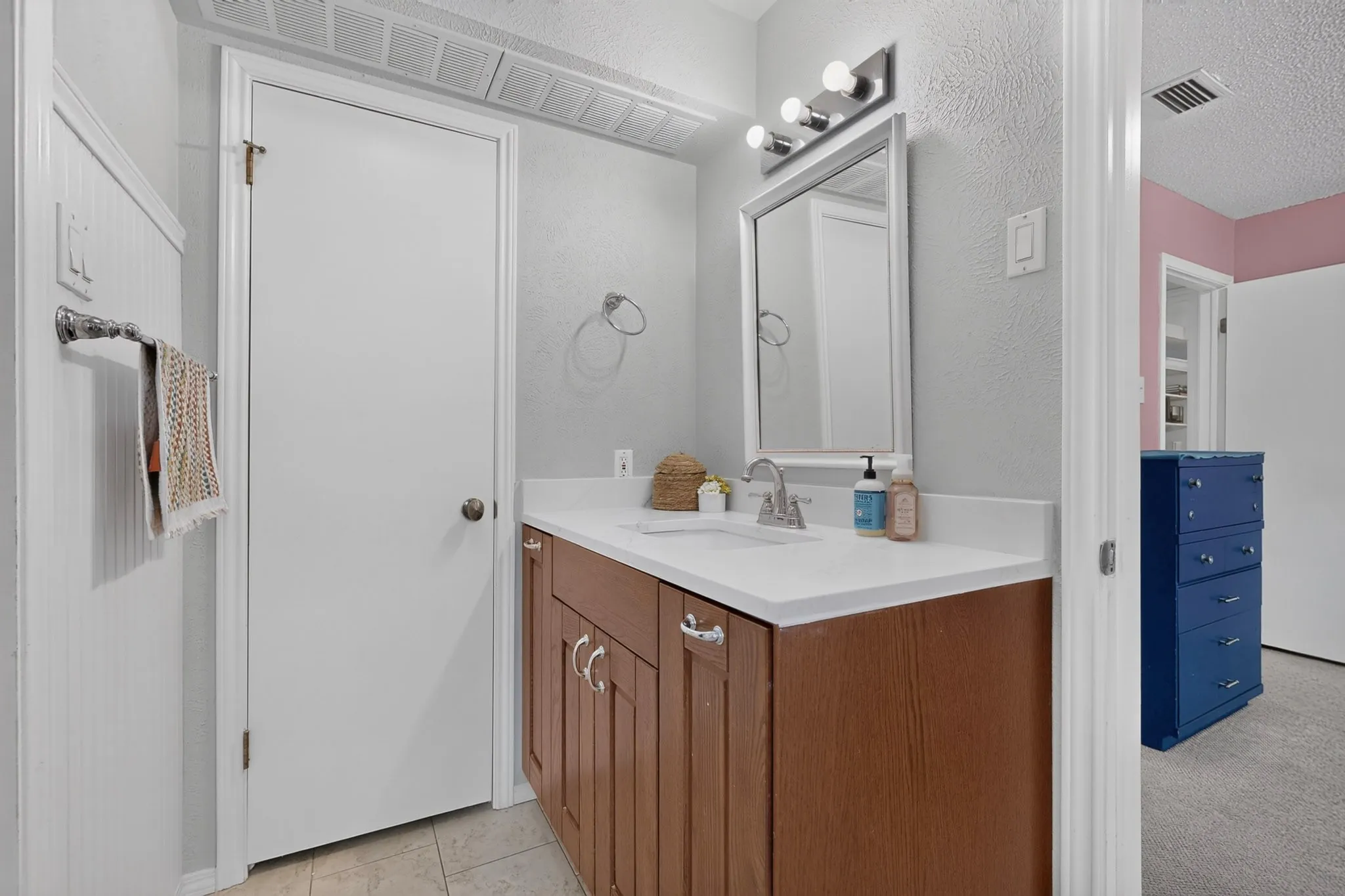 Bathroom vanity featuring a single basin sink, white countertop, wood-finish cabinetry, and chrome hardware