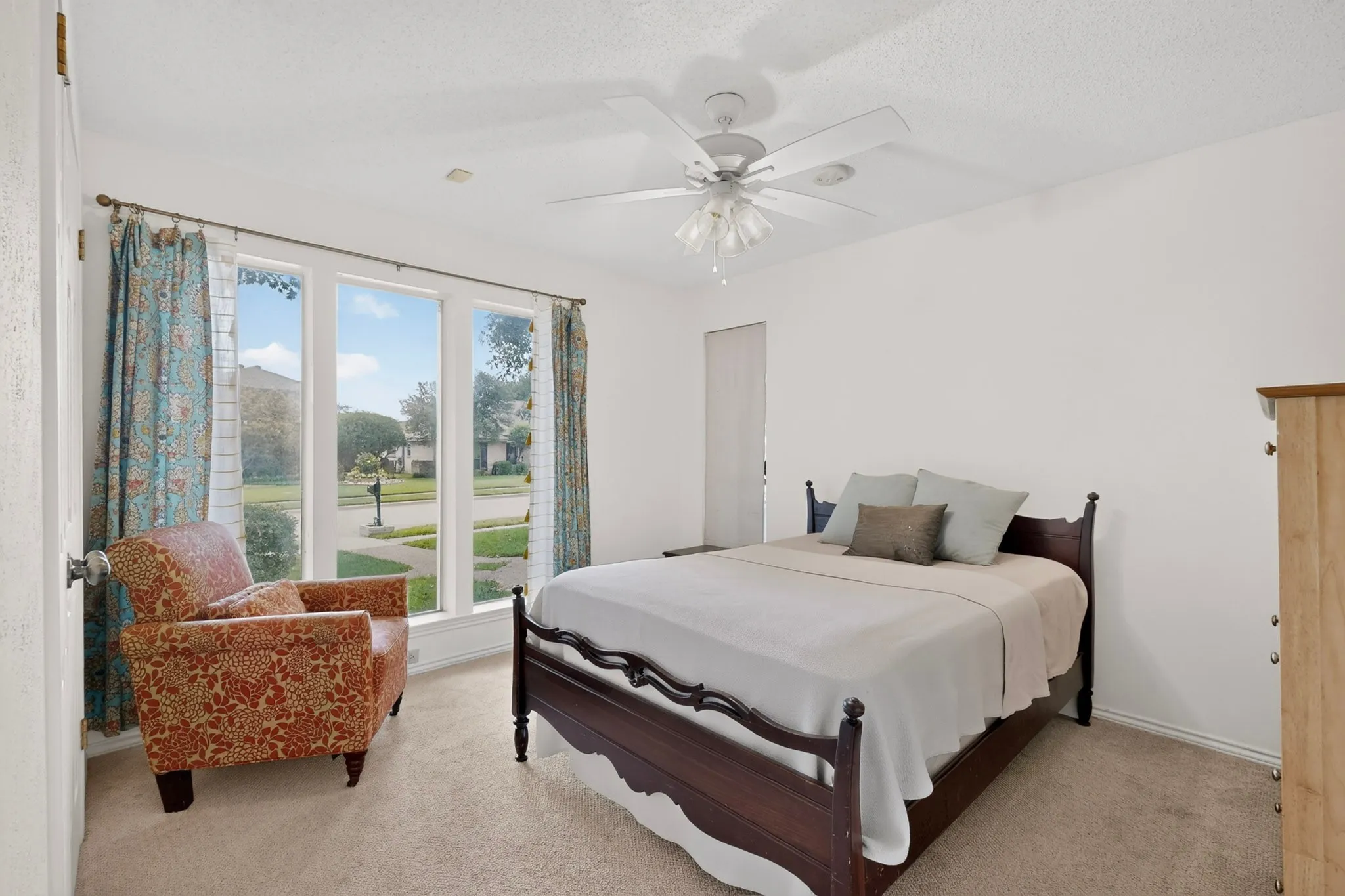 Carpeted room featuring a ceiling fan with light fixture and a three-panel window overlooking the street