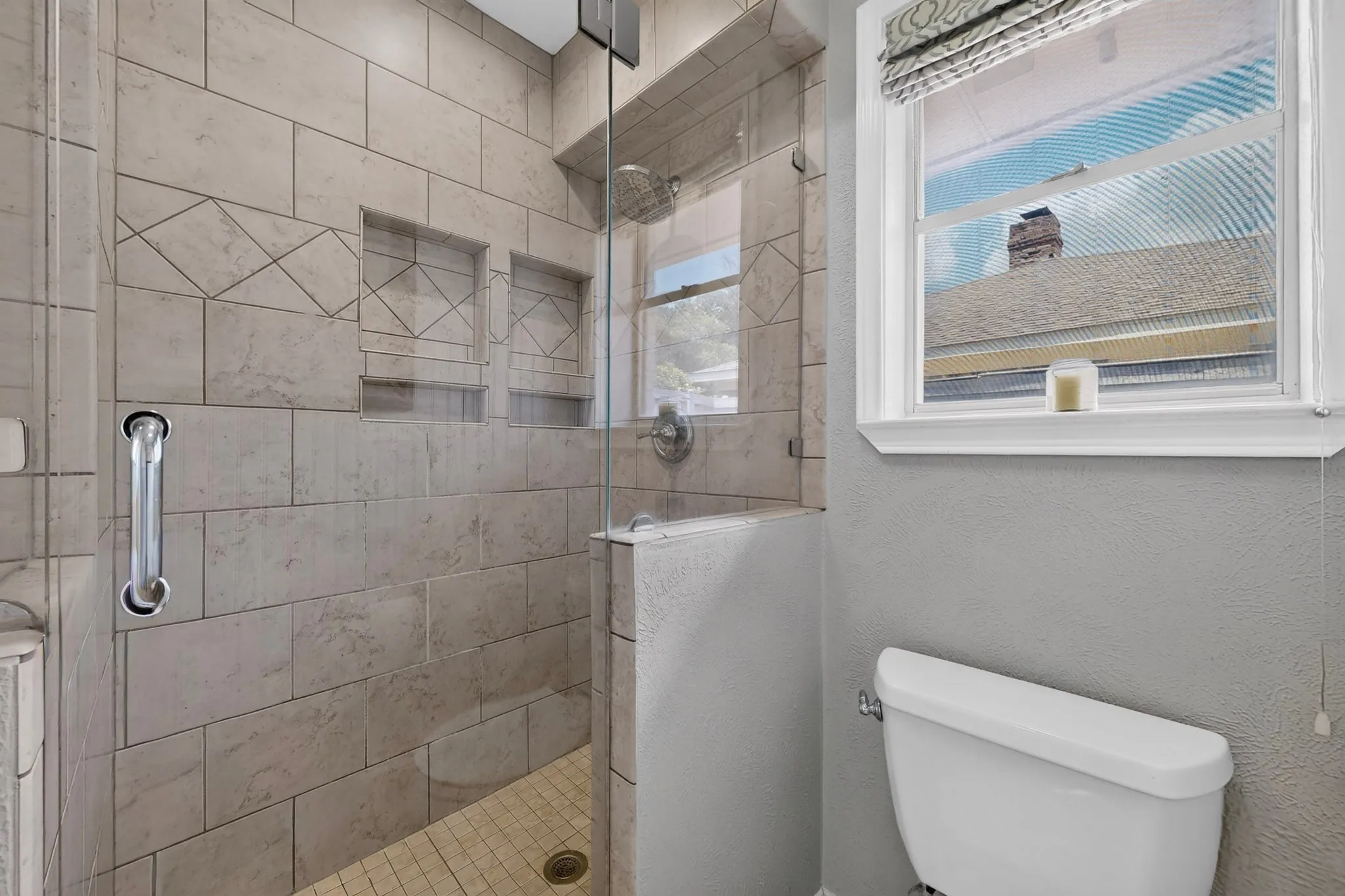 Walk-in shower featuring light-toned tile, glass enclosure, dual built-in shower niches, and a rainfall showerhead
