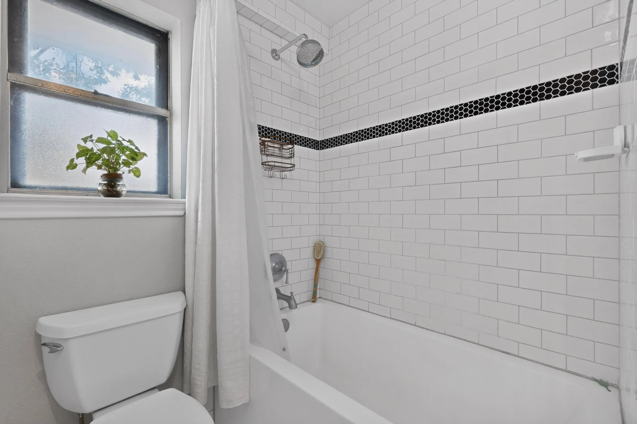 Bathroom featuring a white subway tile shower surround with a black hexagonal accent band, a tub/shower combination, and a white toilet
