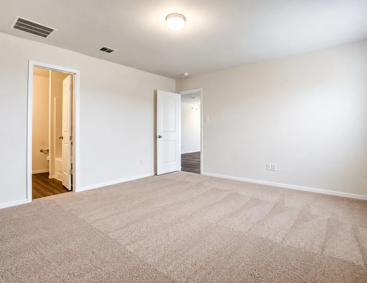 Spacious room with neutral-toned carpet flooring and white baseboards