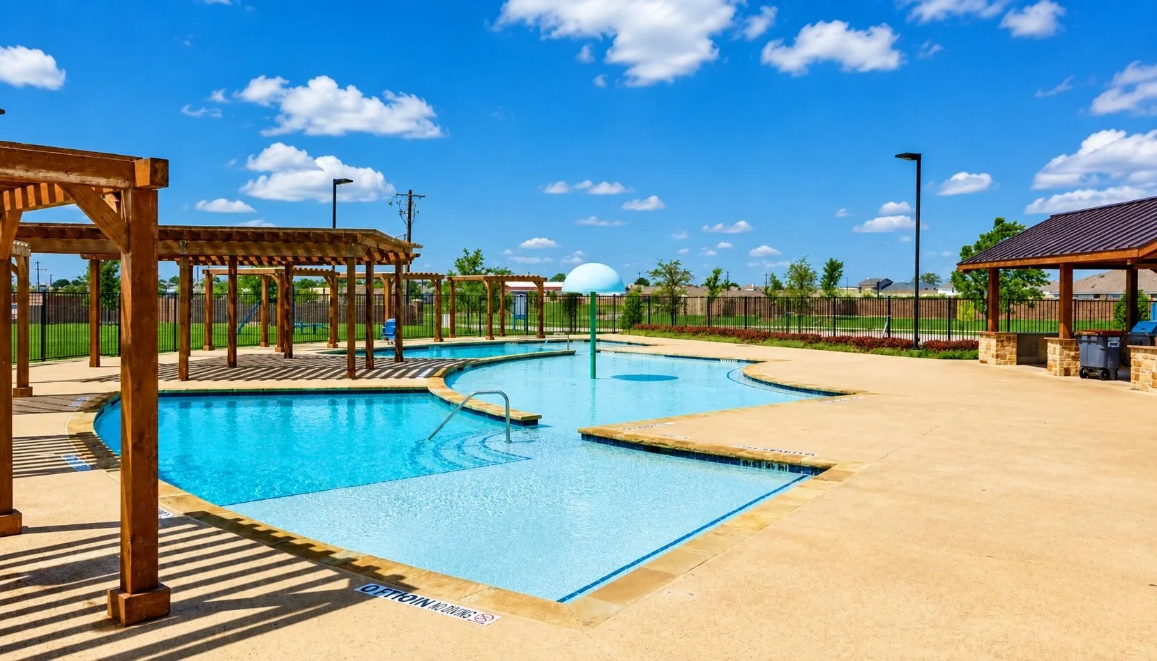 Community swimming pool with concrete decking, a wading area, and a splash pad feature