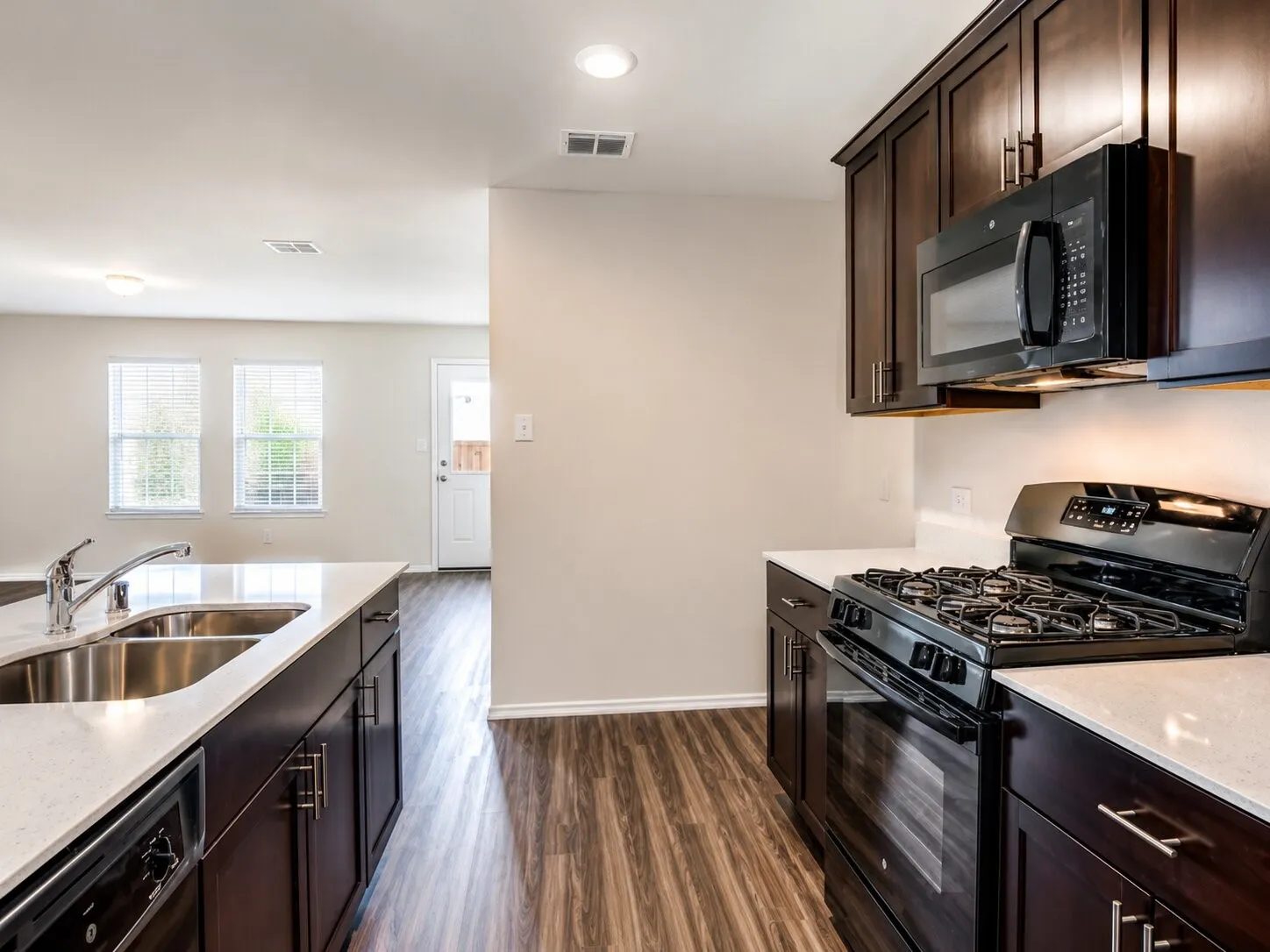 Contemporary kitchen featuring dark wood cabinetry, white countertops, stainless steel double basin sink with a chrome faucet, black gas range, and built-in microwave
