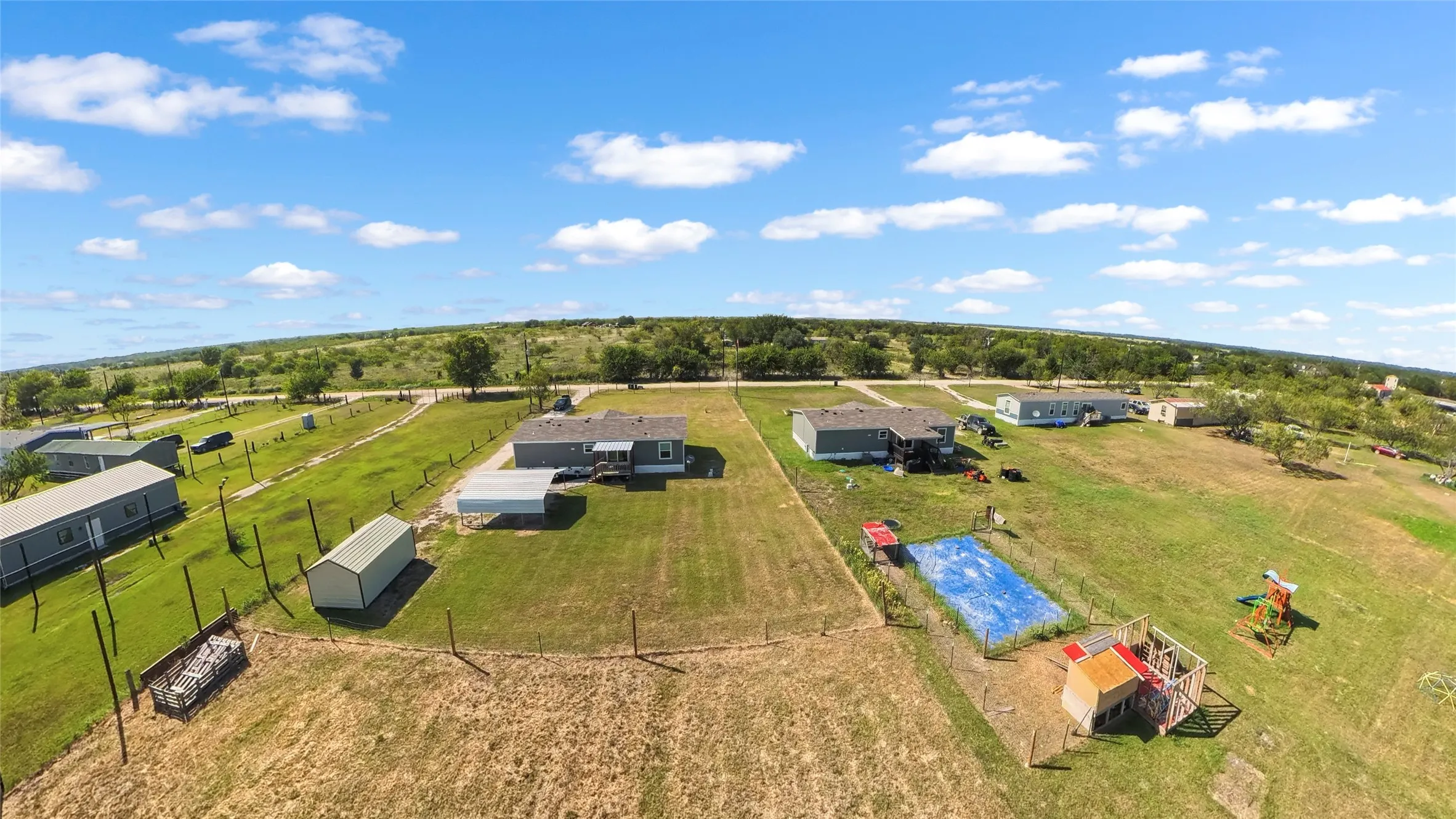 Expansive property featuring multiple single-story residences, open green spaces, and a storage shed