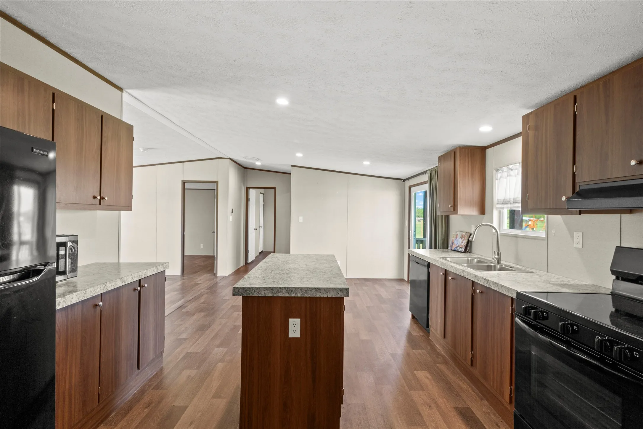 Open-concept kitchen with wood-finish flooring, dark wood cabinetry, and light speckled countertops