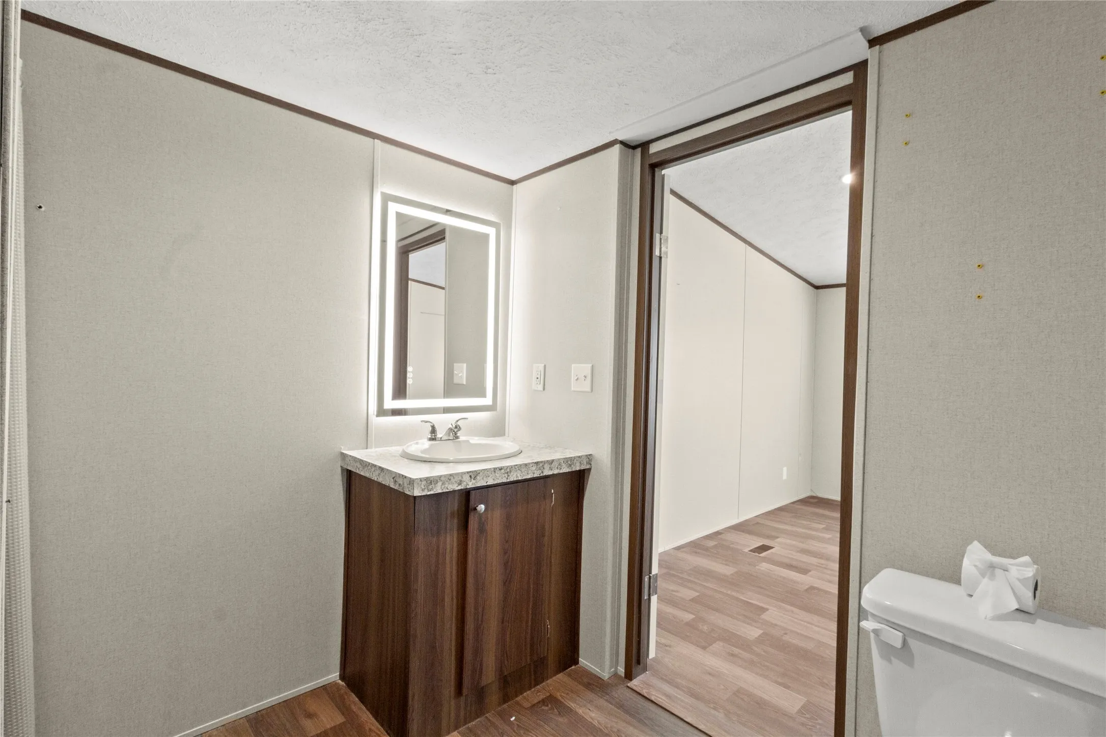 Bathroom vanity featuring a wood-finish cabinet, light countertop, and an illuminated mirror