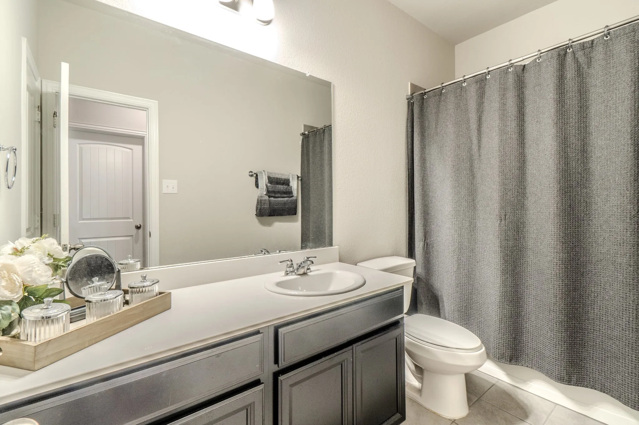 Secondary Bathroom featuring a black vanity with an integrated sink, a large wall-mounted mirror, and tile flooring