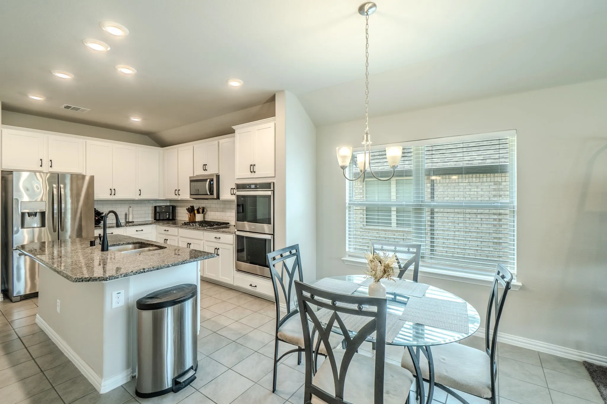 Kitchen featuring white cabinetry, stainless steel appliances, a granite-topped island with an undermount sink, recessed lighting, and tile flooring