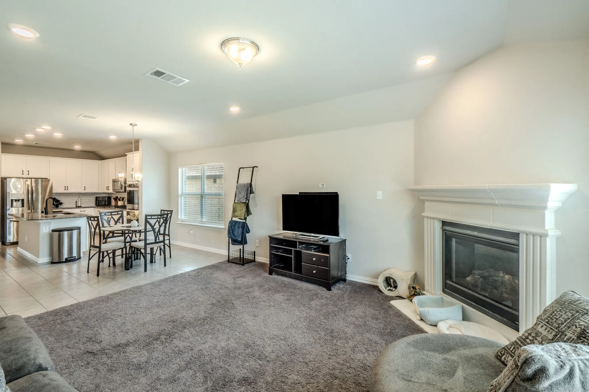 Open-concept living area featuring a fireplace with a detailed mantel, recessed lighting, and tile flooring