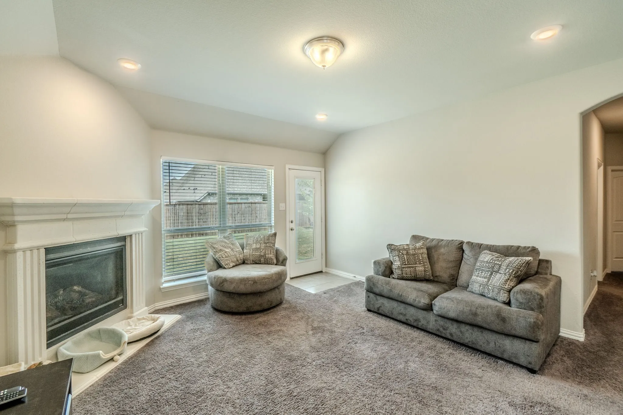 Living room featuring a fireplace with a white mantel, recessed lighting, and a window with horizontal blinds