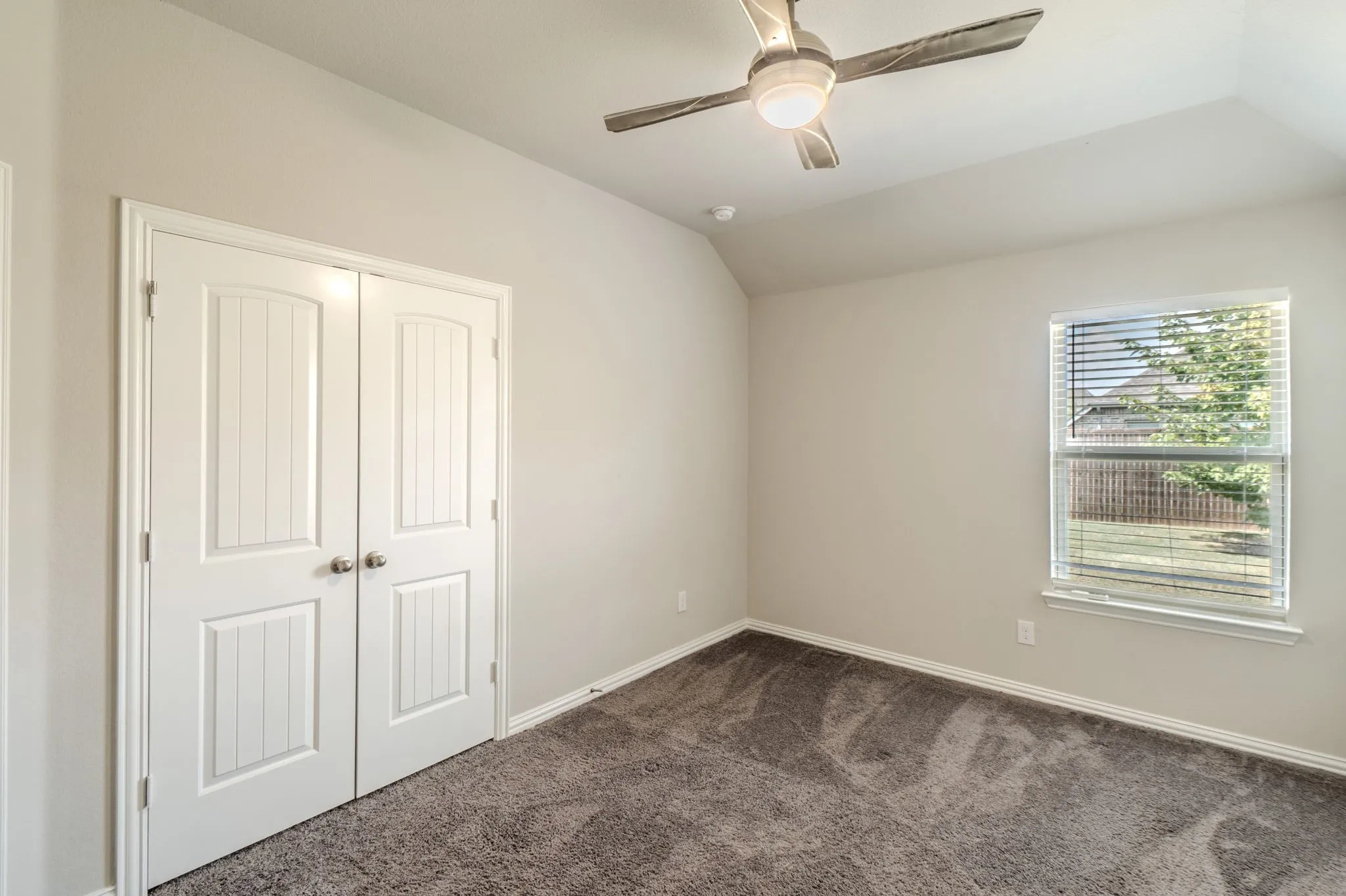 Bedroom featuring vaulted ceiling, neutral wall paint, gray carpet flooring, a ceiling fan with integrated lighting, and a double-pane window with blinds