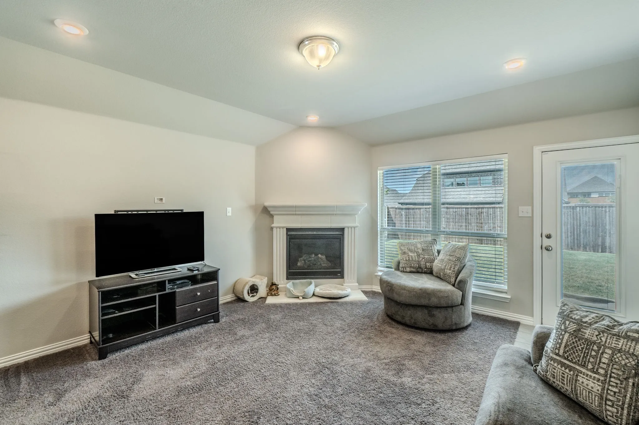 Spacious living area featuring a corner fireplace with a white mantel, recessed lighting, and ample natural light from large windows
