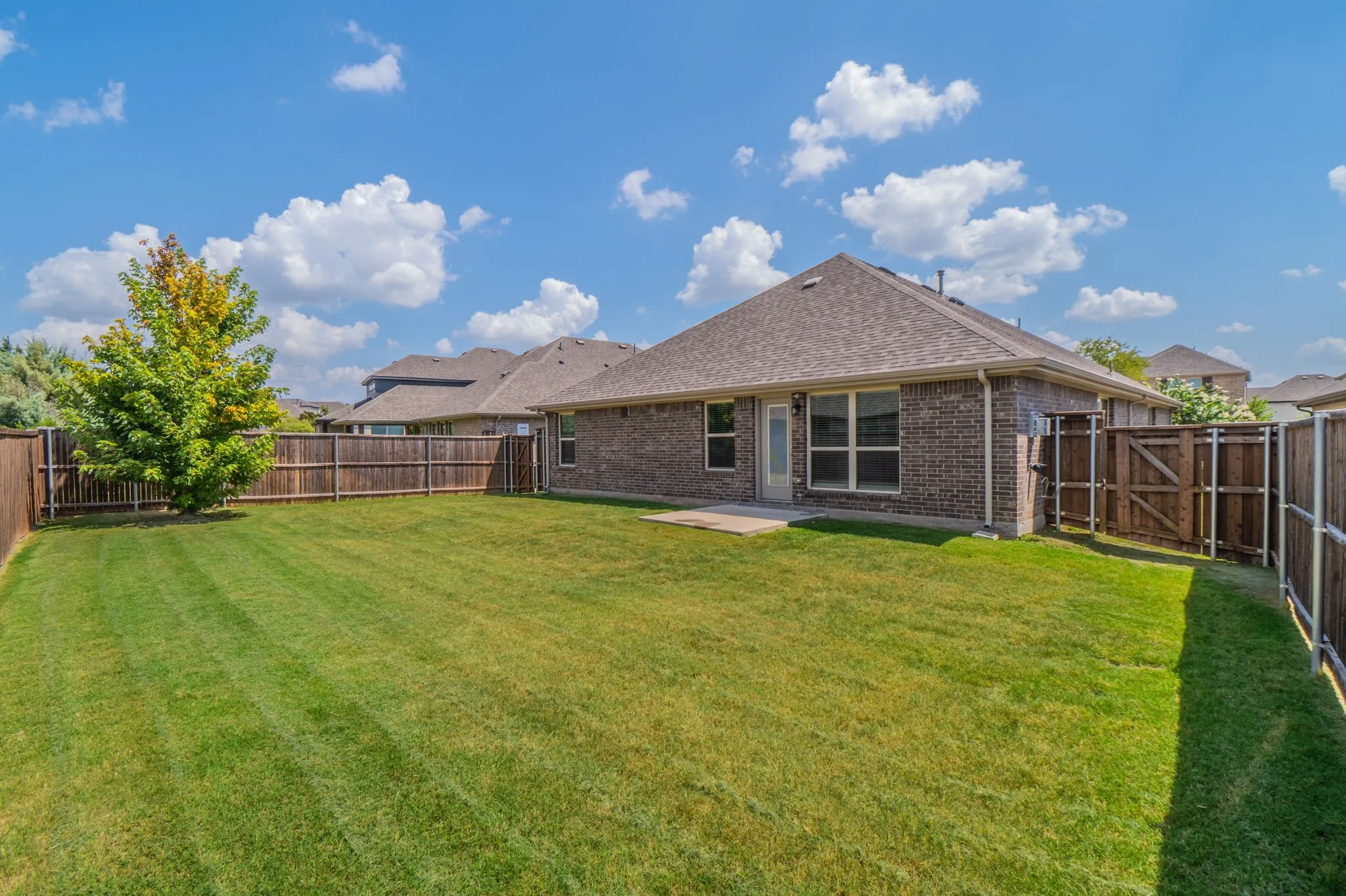 Expansive backyard featuring a manicured lawn, a mature tree, and a full privacy fence