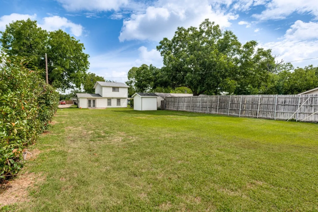 Large grassy yard with detached storage shed, a privacy fence, and mature perimeter foliage