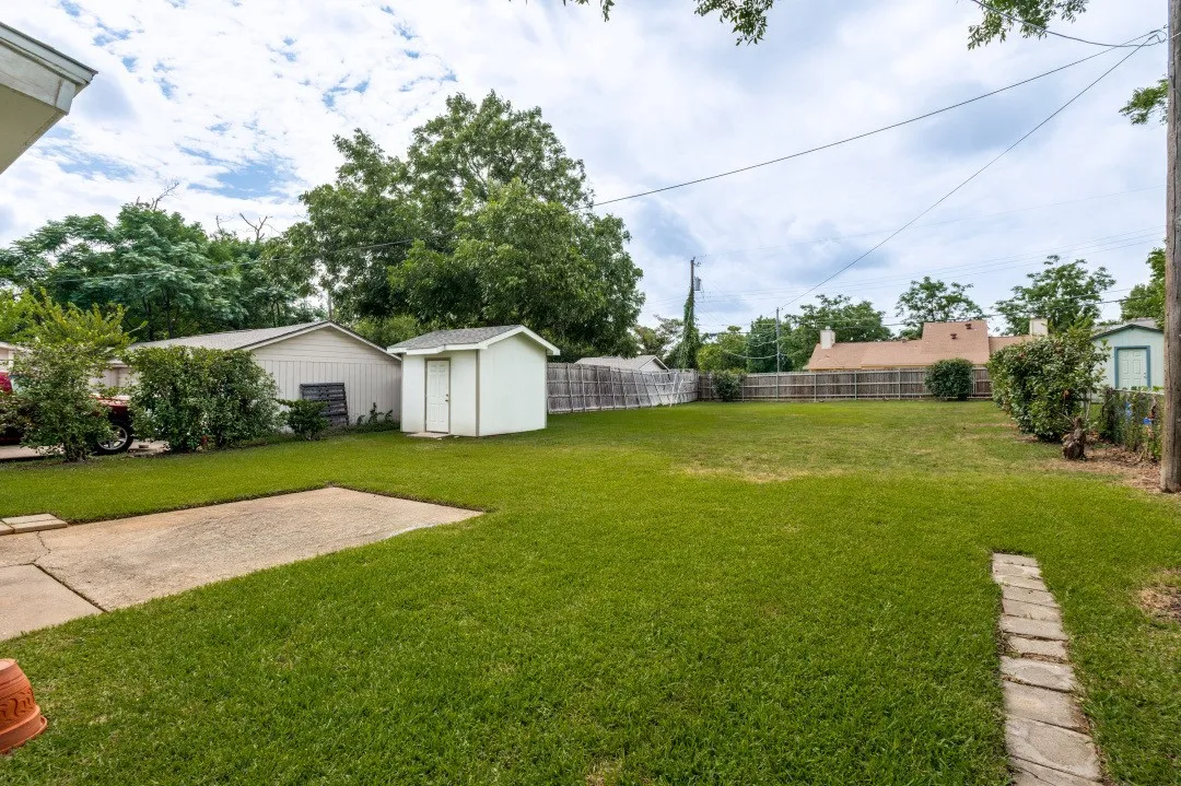 Expansive backyard featuring a lush lawn, concrete patio area, and storage shed