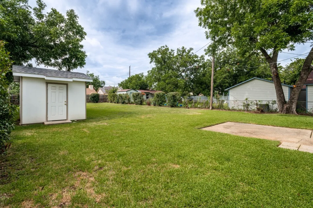 Spacious backyard featuring a storage shed with a shingle roof and concrete pad
