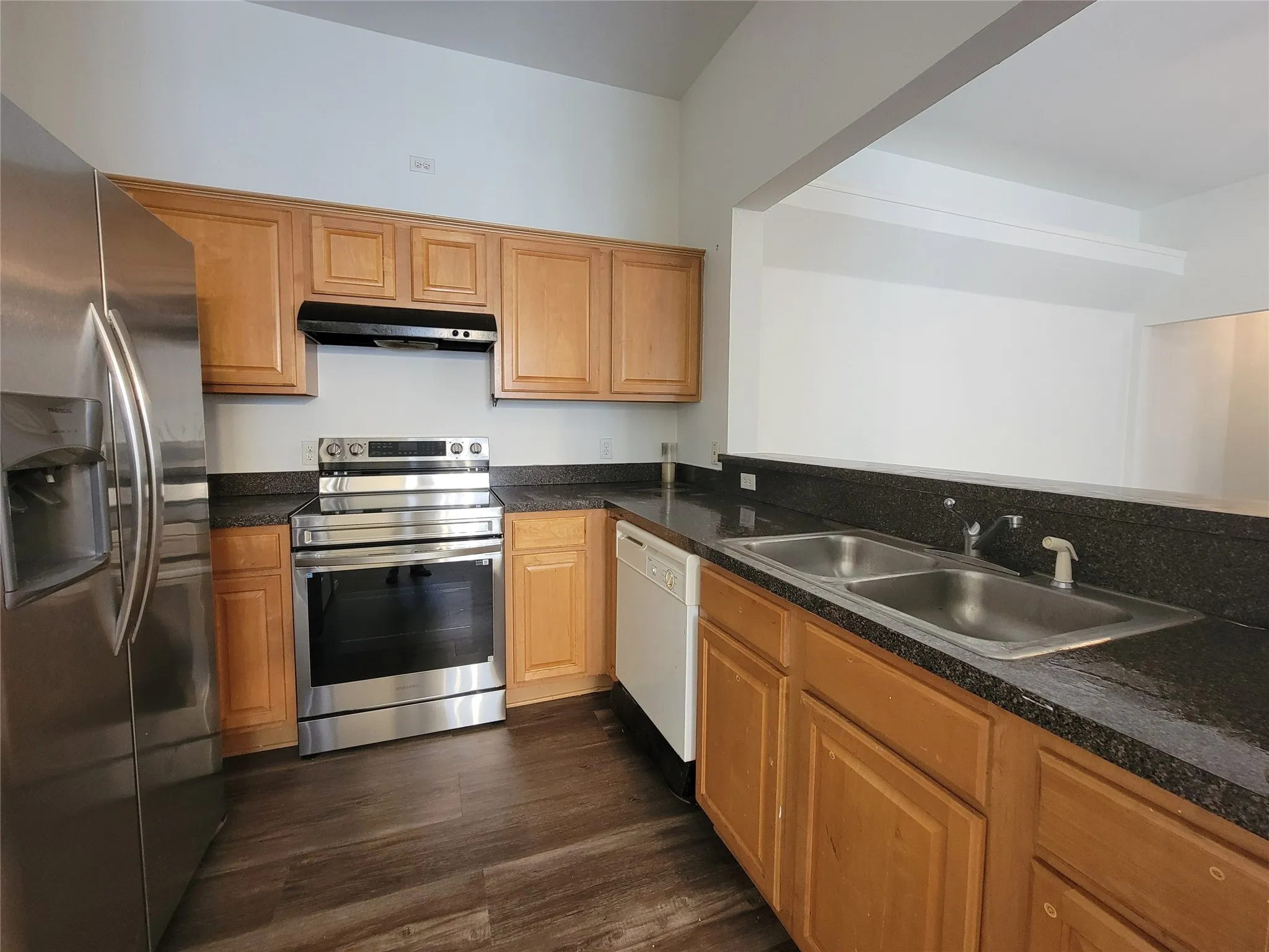 Kitchen featuring wood-finish cabinetry, dark countertops, stainless steel refrigerator, stainless steel range, and a double basin sink