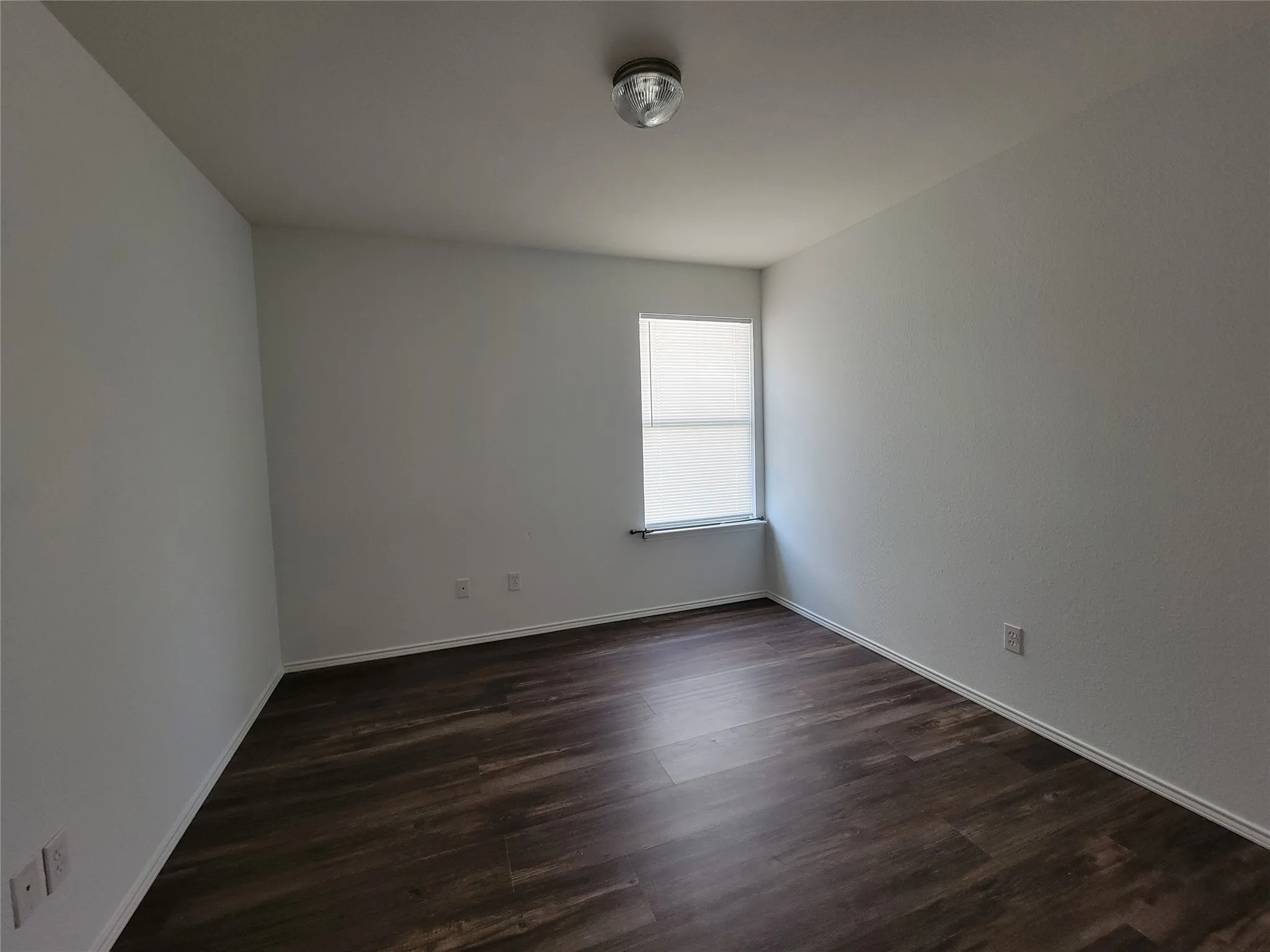 Room featuring wood-finish flooring, white walls, a single window with blinds, and a flush-mount ceiling light fixture