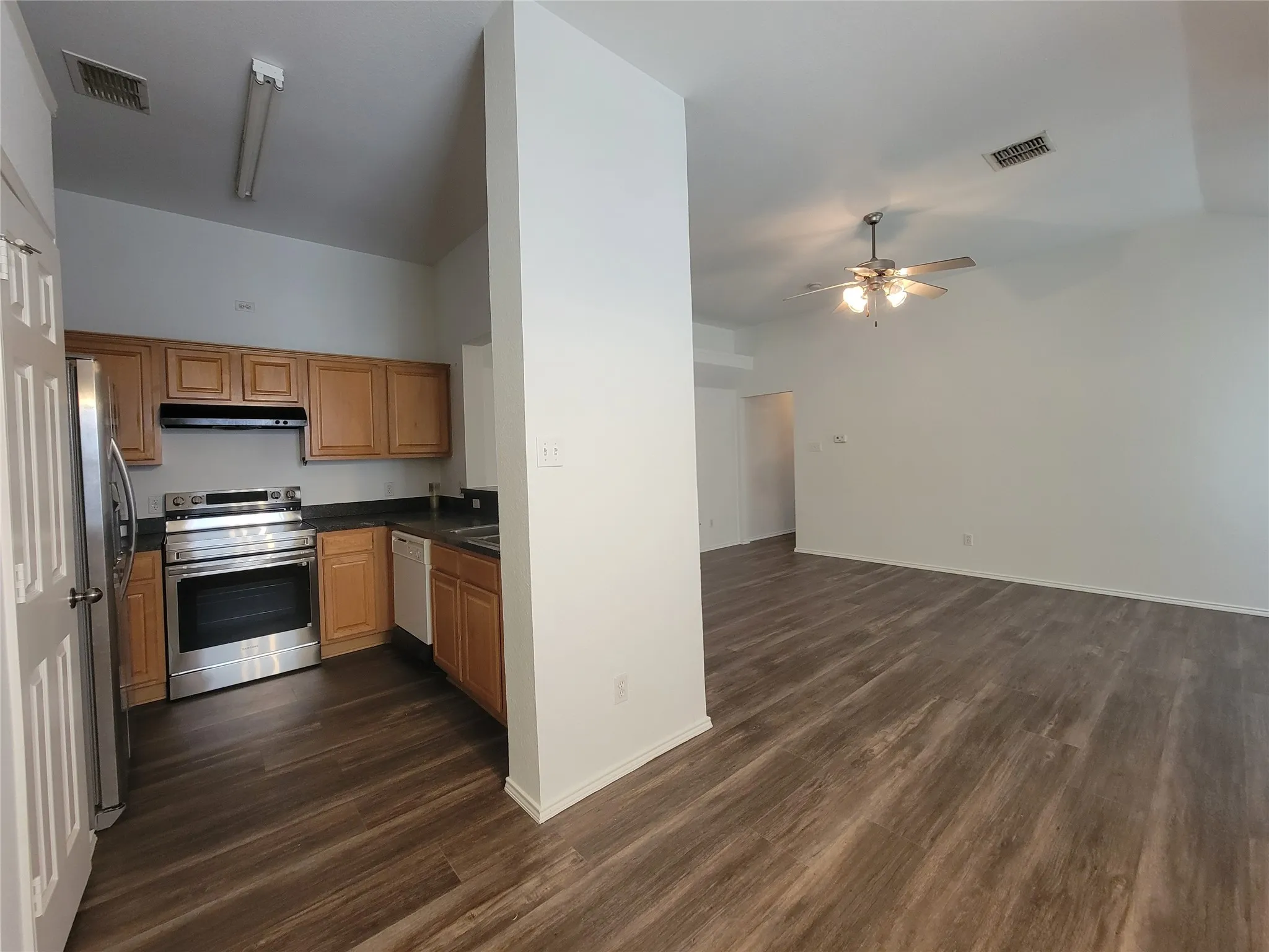 Open-concept living space featuring wood-finish flooring, a contemporary ceiling fan, and a kitchen with stainless steel appliances, wood cabinetry, and dark countertops