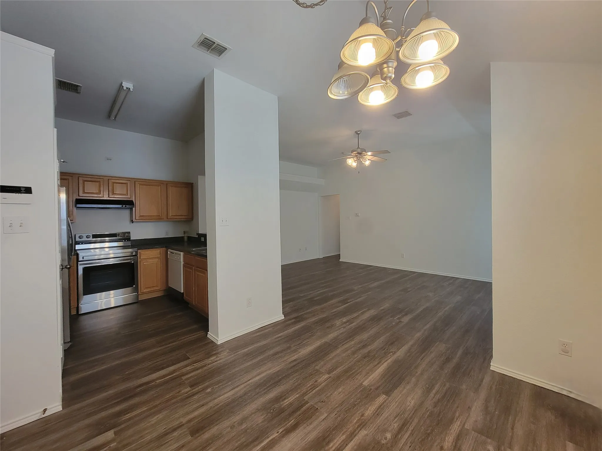 Open-concept living space featuring wood-finish flooring, a kitchen with stainless steel appliances, wood cabinetry, and a ceiling fan