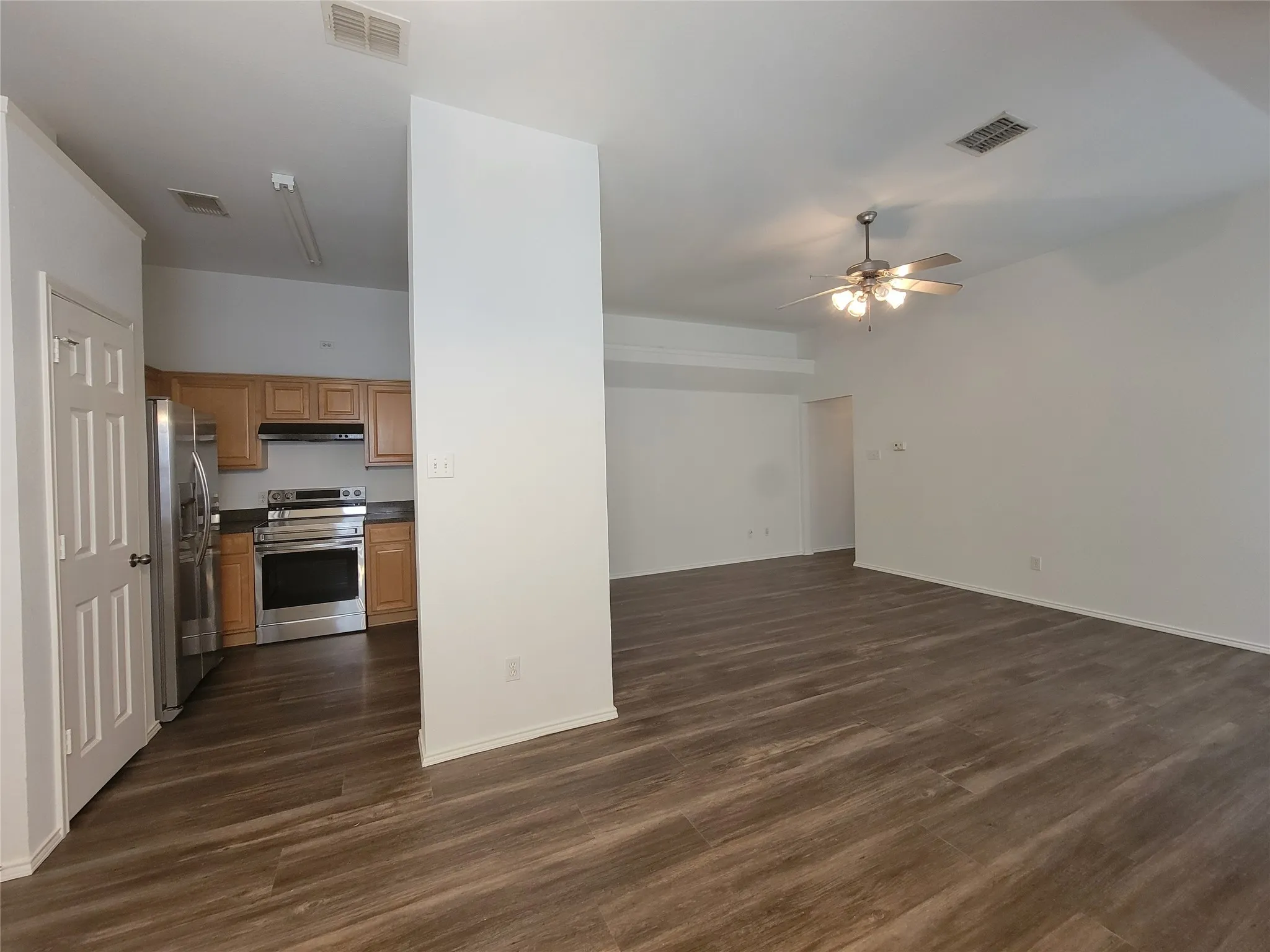 Spacious living area featuring wood-finish flooring, a ceiling fan with integrated lighting, and a neutral color palette