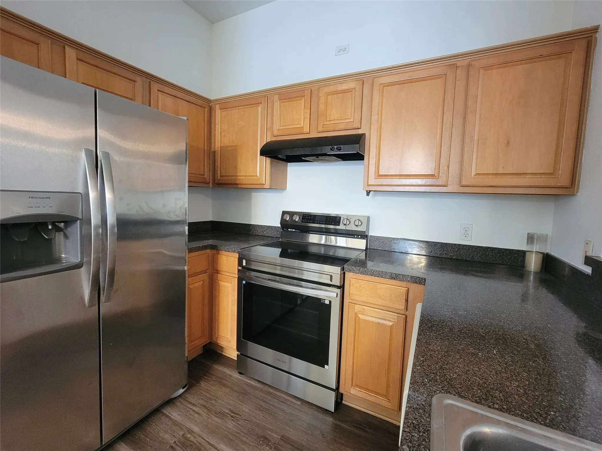 Kitchen featuring stainless steel appliances, wood-finish cabinetry, dark speckled countertops, and wood-finish flooring