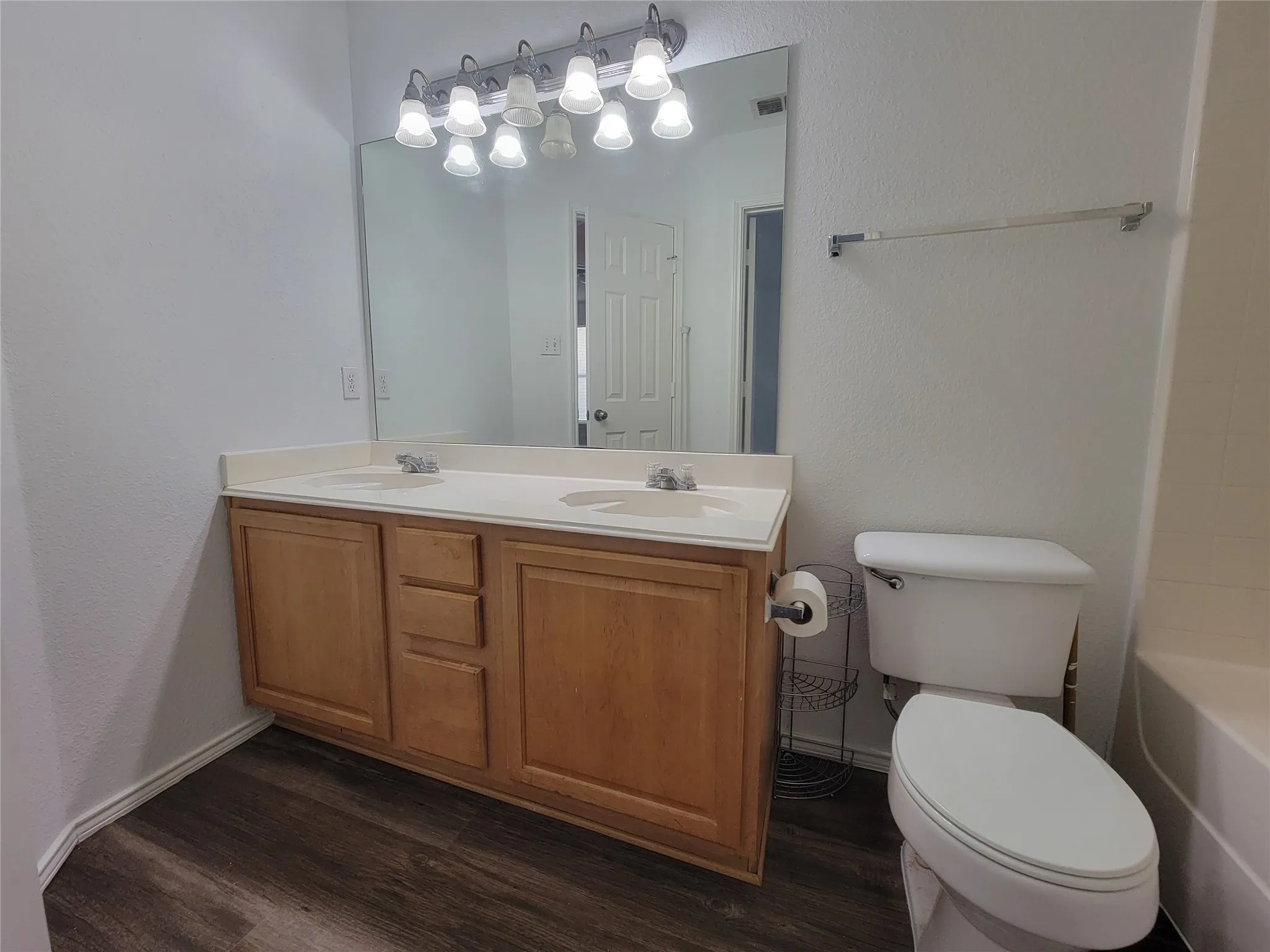 Bathroom featuring a dual vanity with light-toned countertops, wood-finish cabinetry, and a large mirror with integrated lighting