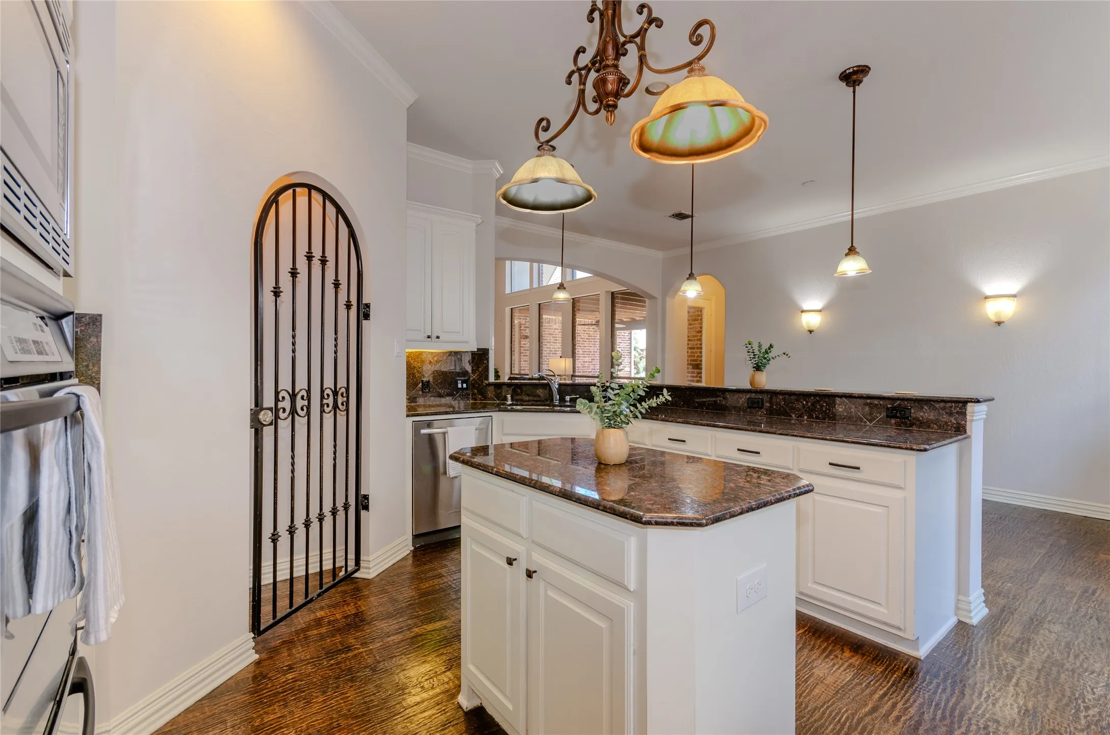 Open-concept living area featuring wood-finish flooring, a contemporary staircase with iron balusters, and a kitchen island with a dark countertop