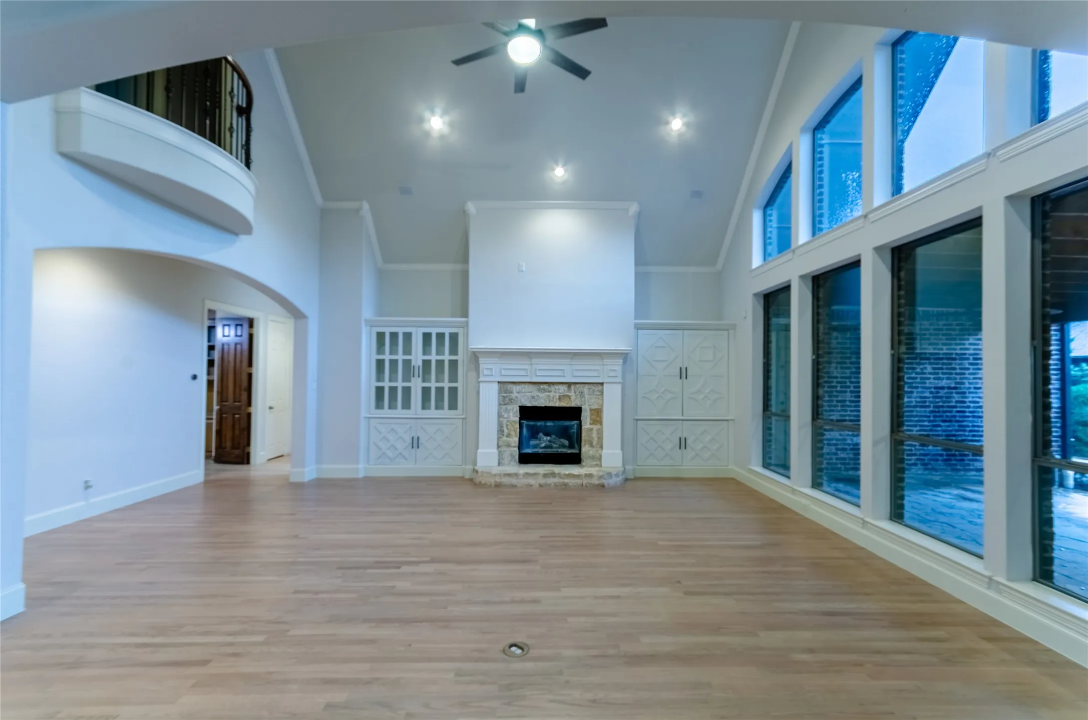 Spacious living area featuring high vaulted ceilings, light wood-finish flooring, and a stone fireplace with a white mantel