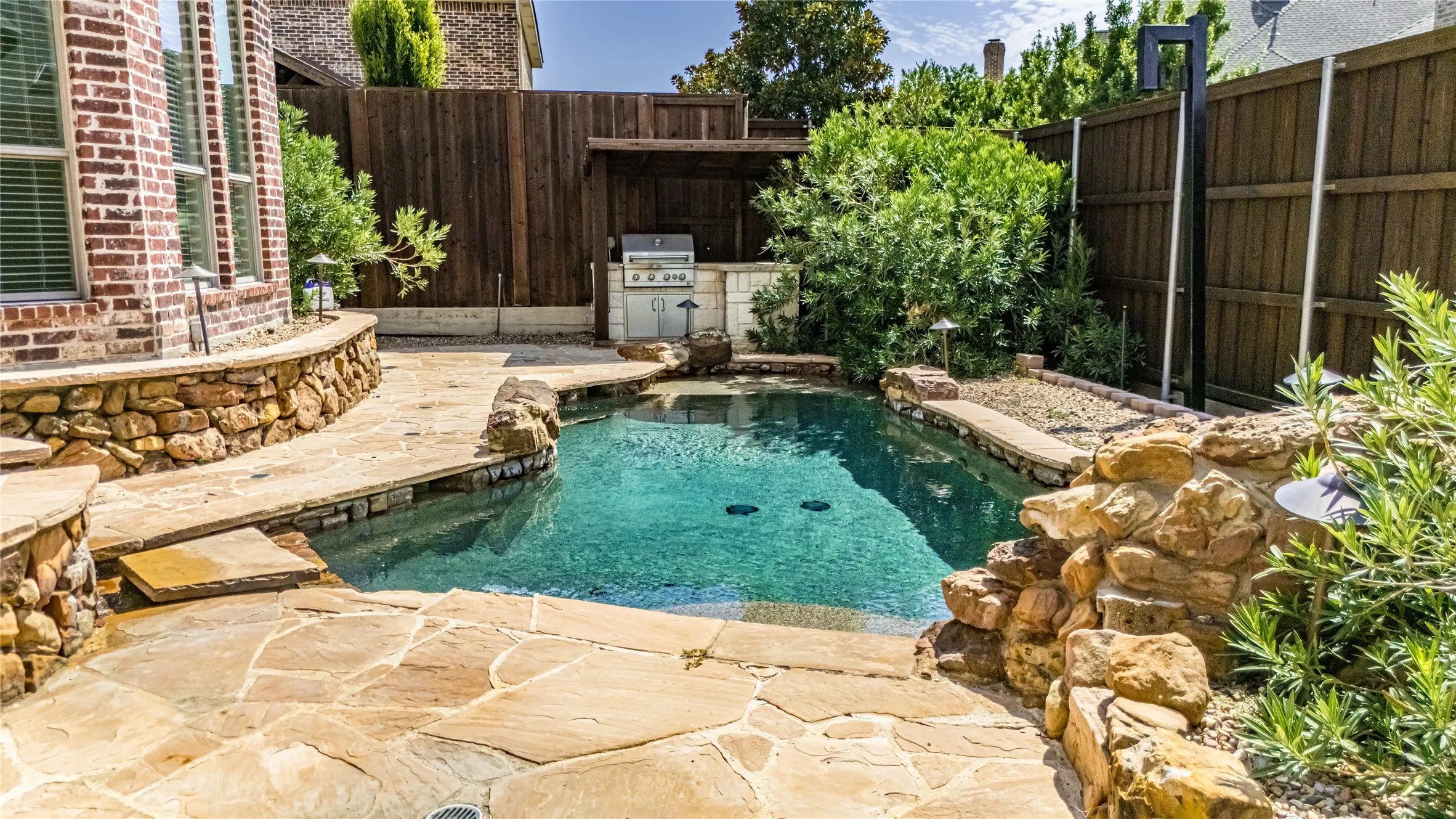 Curved swimming pool with natural stone coping and rock features, surrounded by flagstone patio pavers