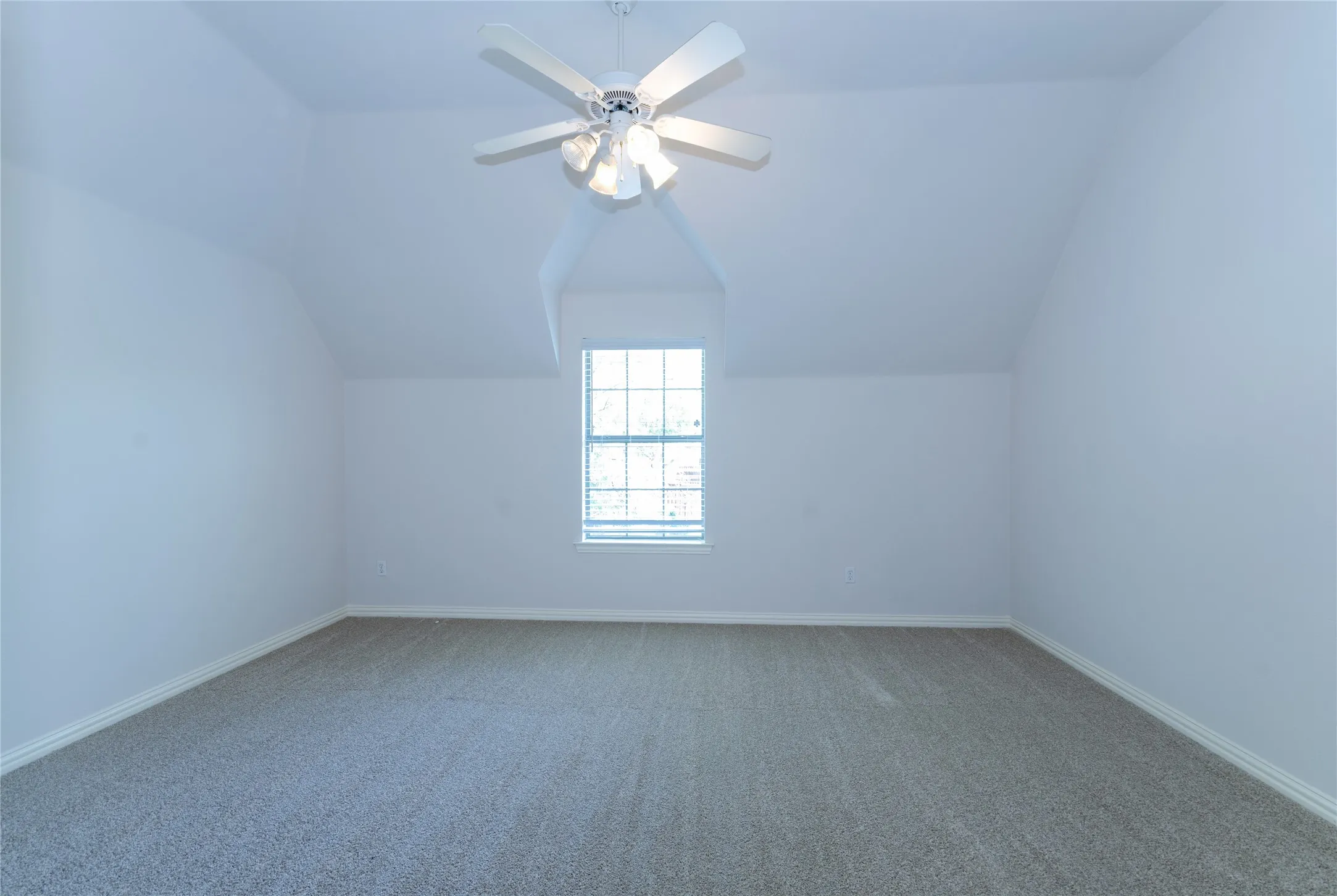 Spacious bedroom # 3 featuring vaulted ceilings, a central ceiling fan with integrated lighting, a large window with horizontal blinds, neutral wall paint, and gray carpet flooring